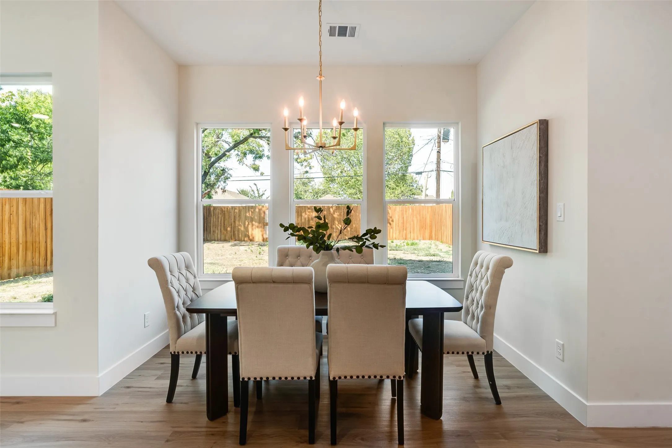 Wood-finish flooring, multiple windows, a brass finish chandelier, and white wall finishes