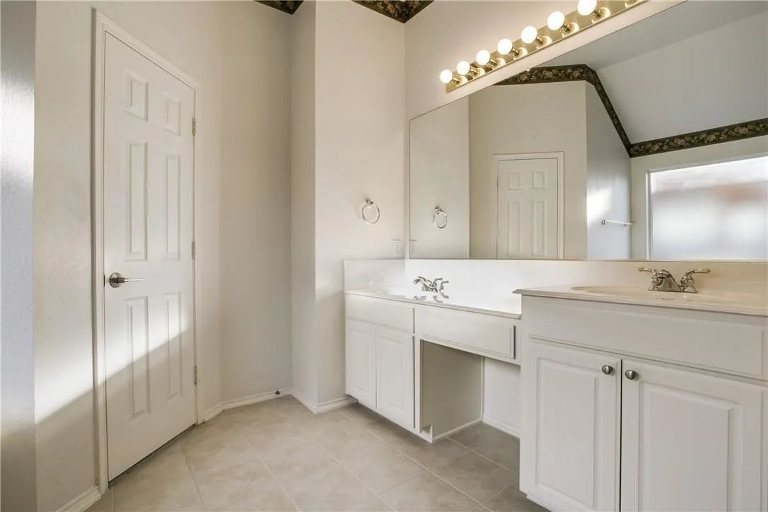 Bathroom with tile patterned floors, vaulted ceiling, and dual bowl vanity
