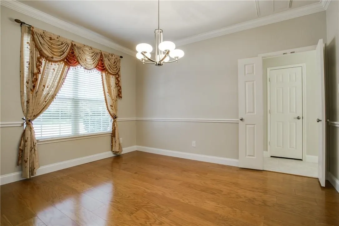 Empty room featuring hardwood / wood-style flooring, a chandelier, and ornamental molding