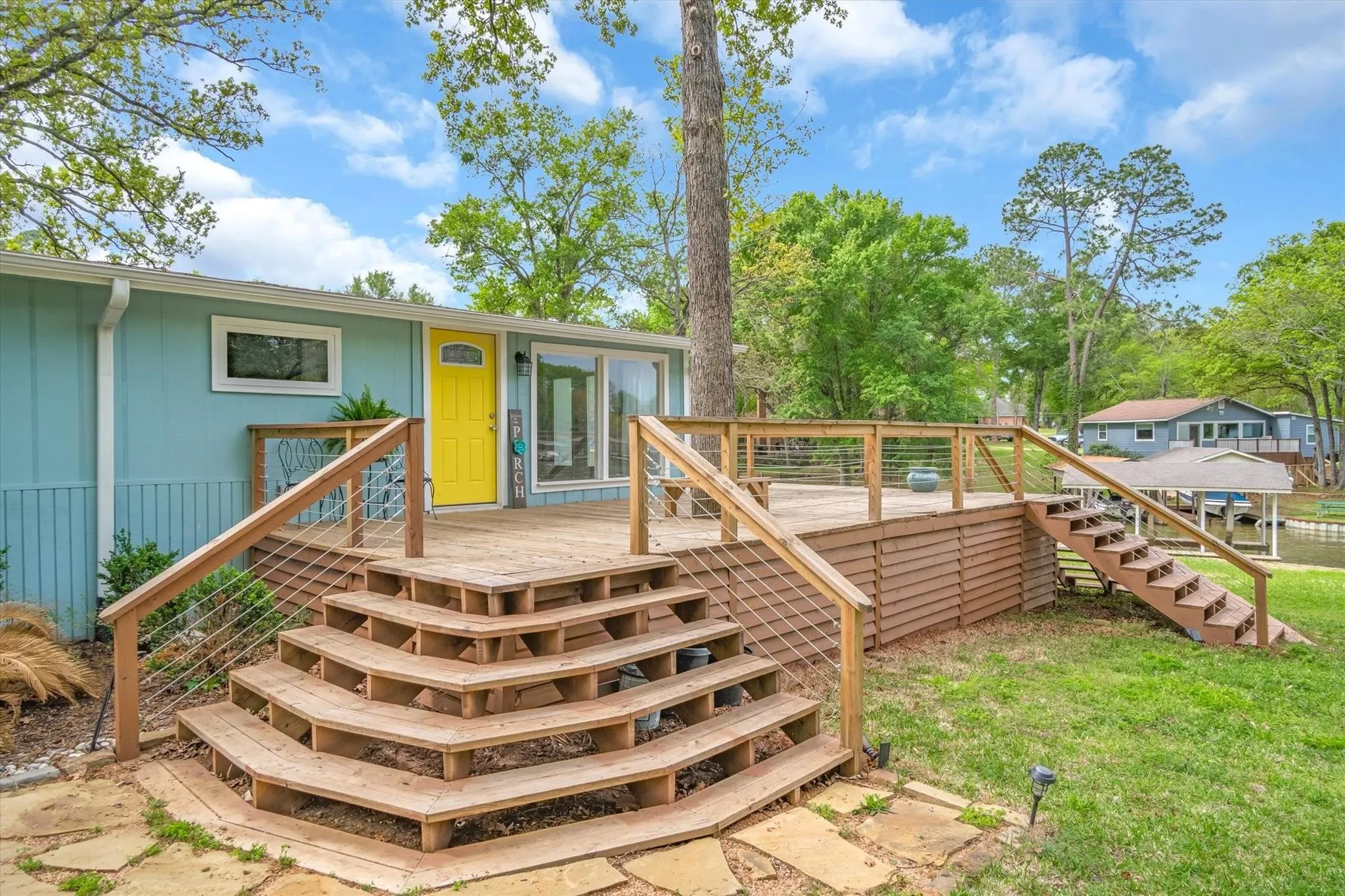 Expansive wood deck with cable railing, multi-tier wood stairs, and direct water access