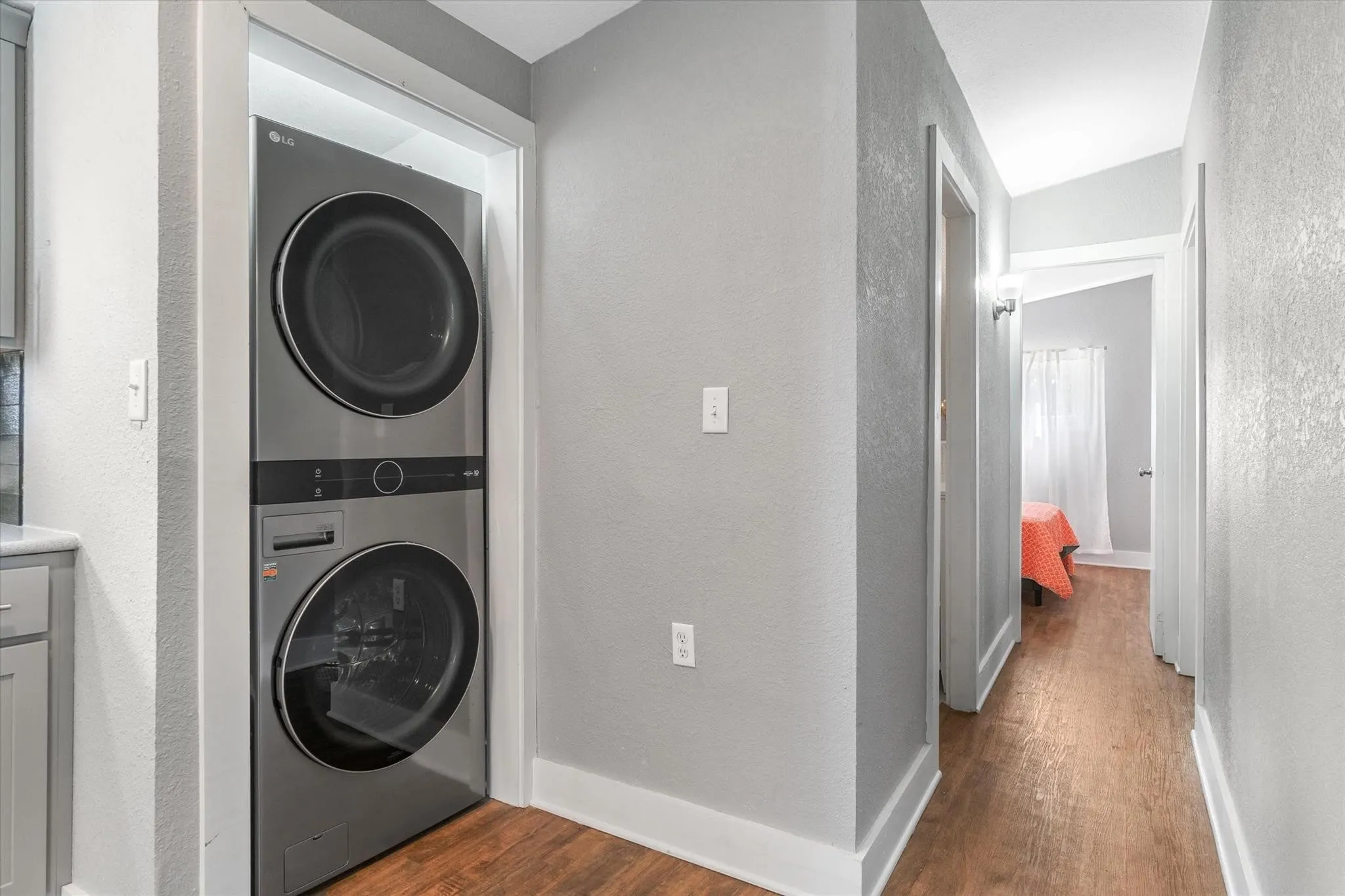 Stackable laundry machines, wood-finish flooring, and wall-mounted light fixture