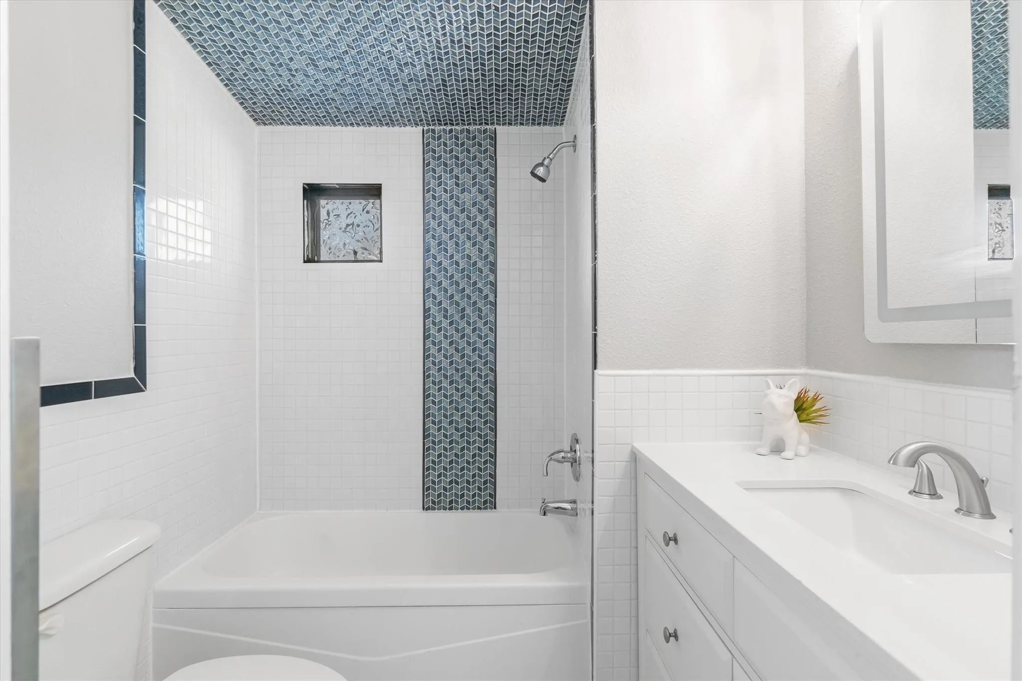 White subway tile surround with contrasting accent tile, built-in shower niche, integrated bathtub, white vanity with undermount sink, and wall-mounted medicine cabinet