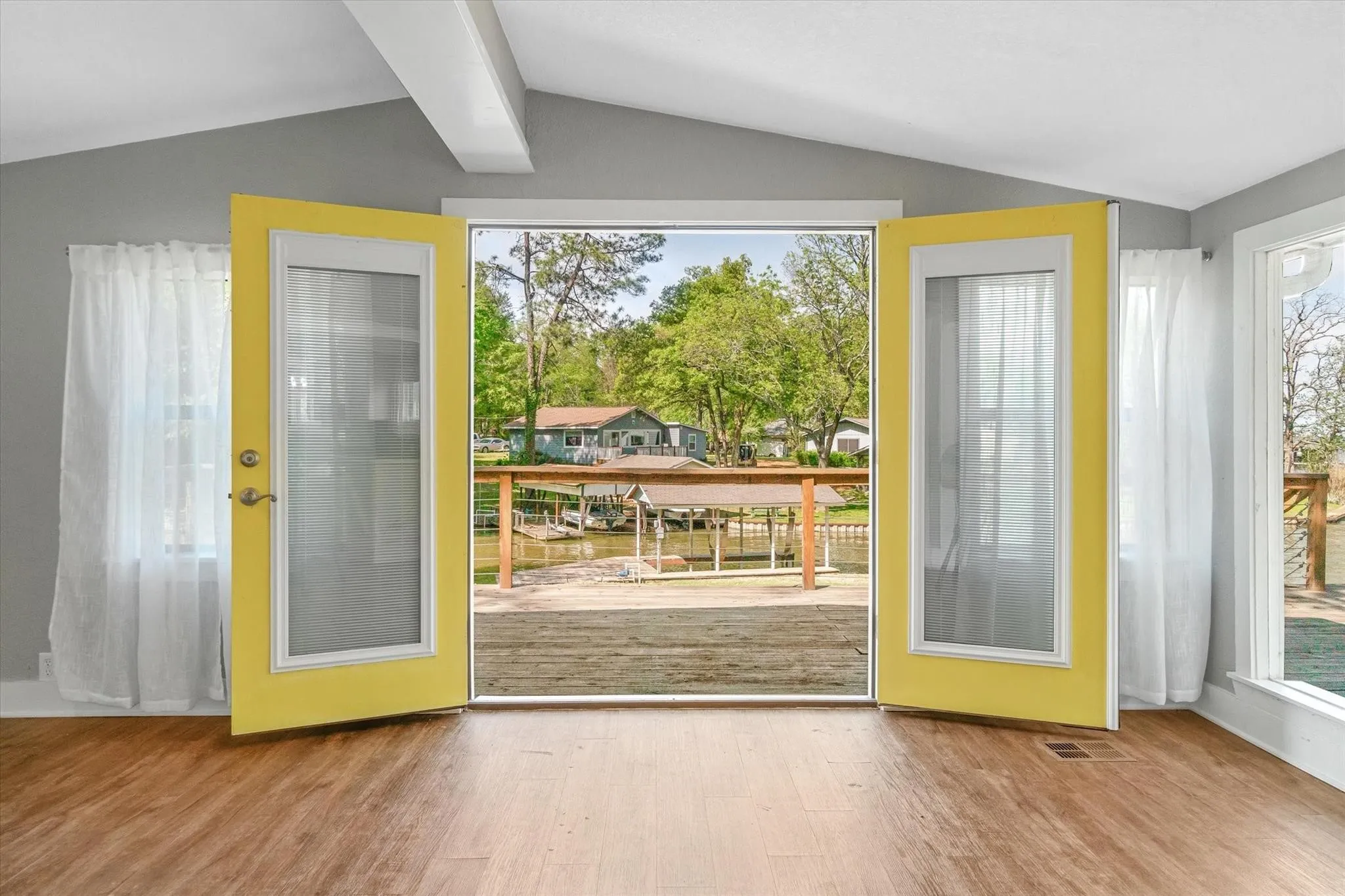 Wood-finish flooring, exposed ceiling beams, and bright yellow French doors opening to a wood-plank deck