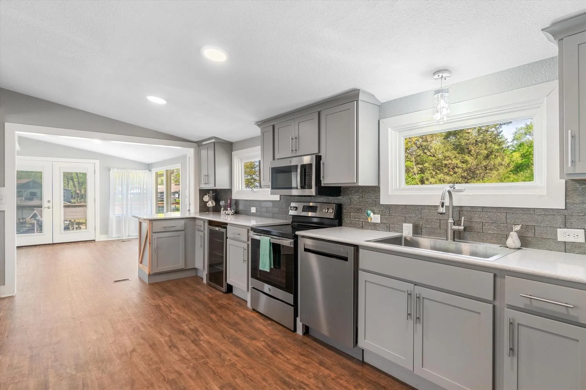 Kitchen featuring light gray cabinetry, stainless steel appliances, light-toned countertops, and a gray tile backsplash