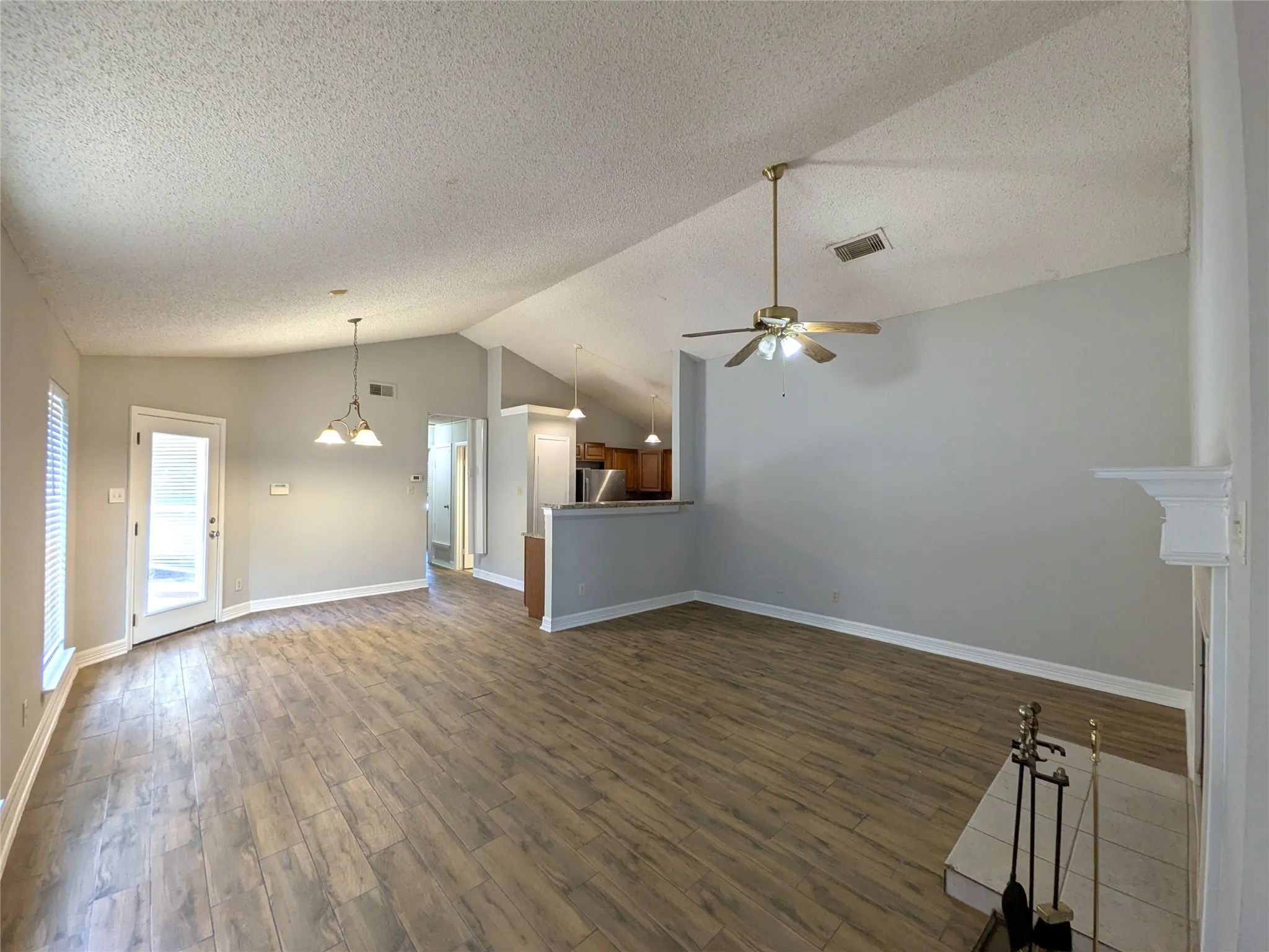 Vaulted ceilings, wood-finish flooring, ceiling fan, and a fireplace with a white mantel