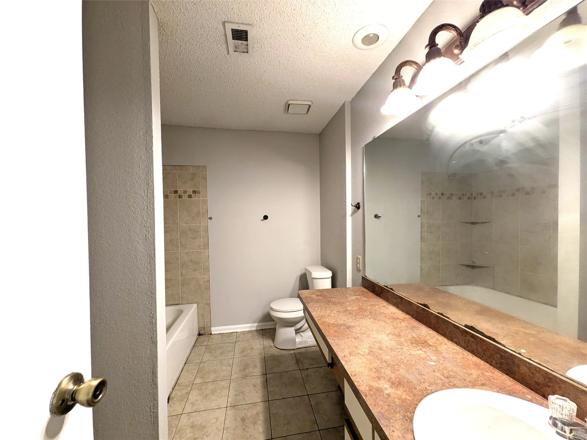 Bathroom featuring a vanity with an integrated sink, a large mirror, and a bathtub with tiled surround