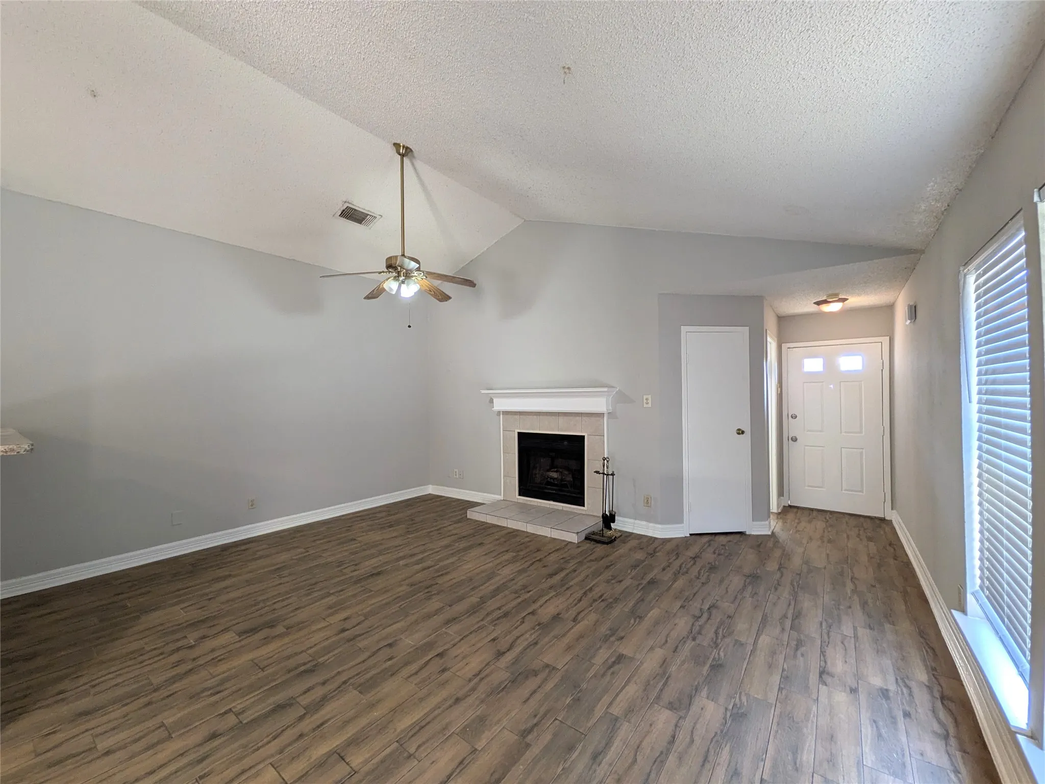 Vaulted ceilings with a ceiling fan, fireplace with a mantel, wood-finish flooring, and white window blinds