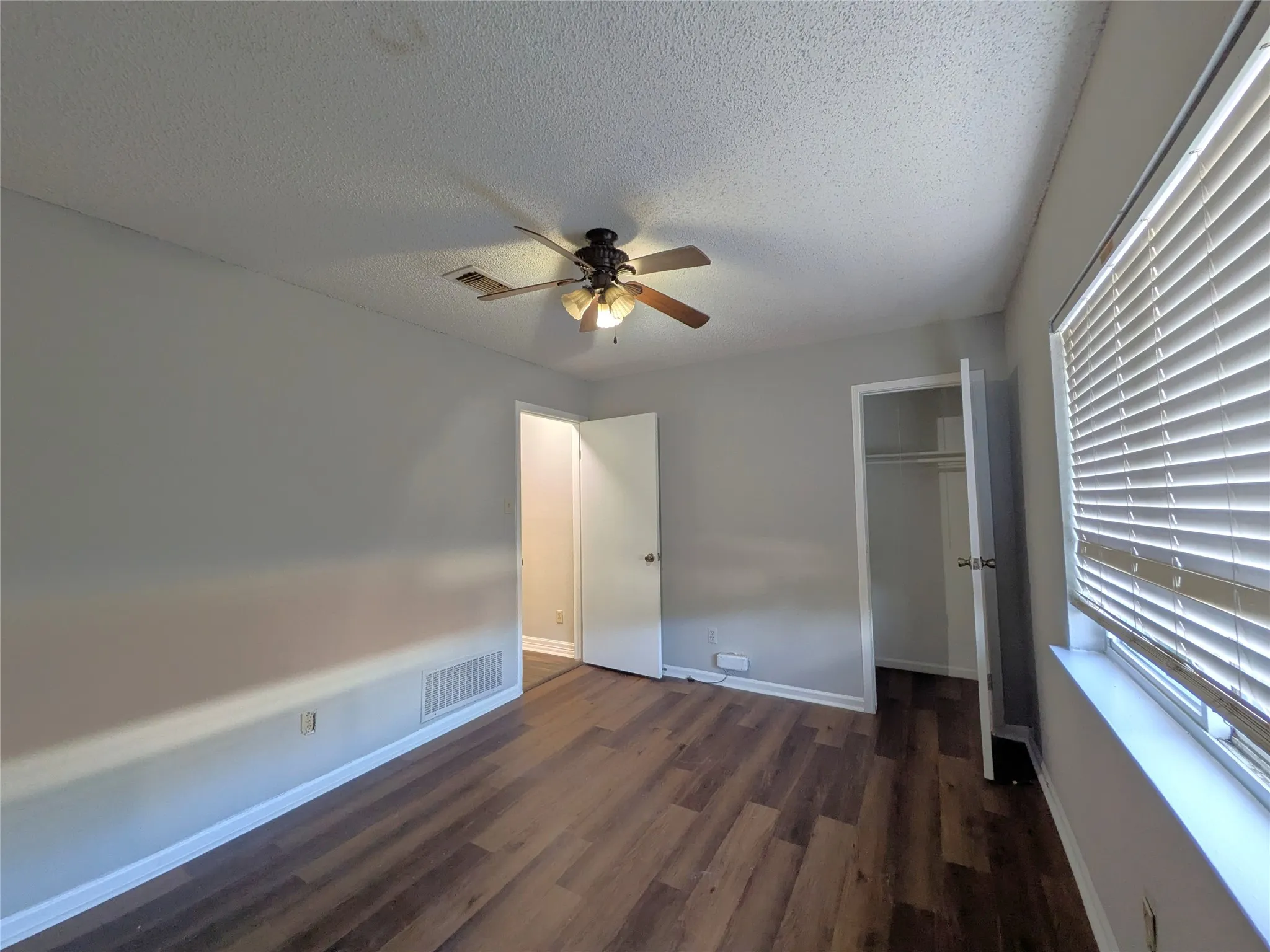Wood-finish flooring, ceiling fan with integrated lighting, window with blinds, and a built-in closet with shelving