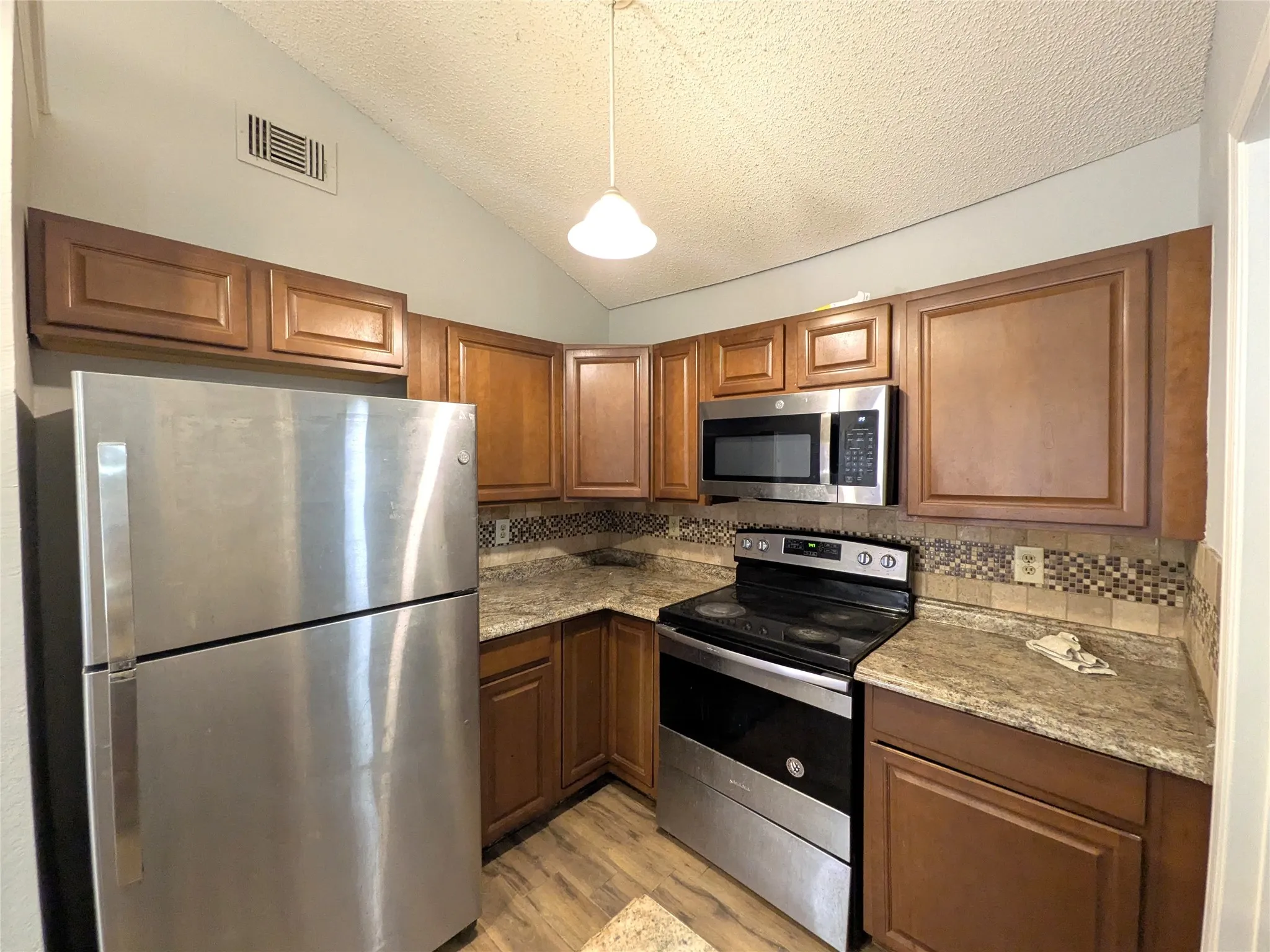 Kitchen featuring wood-finish cabinetry, stainless steel appliances, speckled countertops, and a decorative tile backsplash