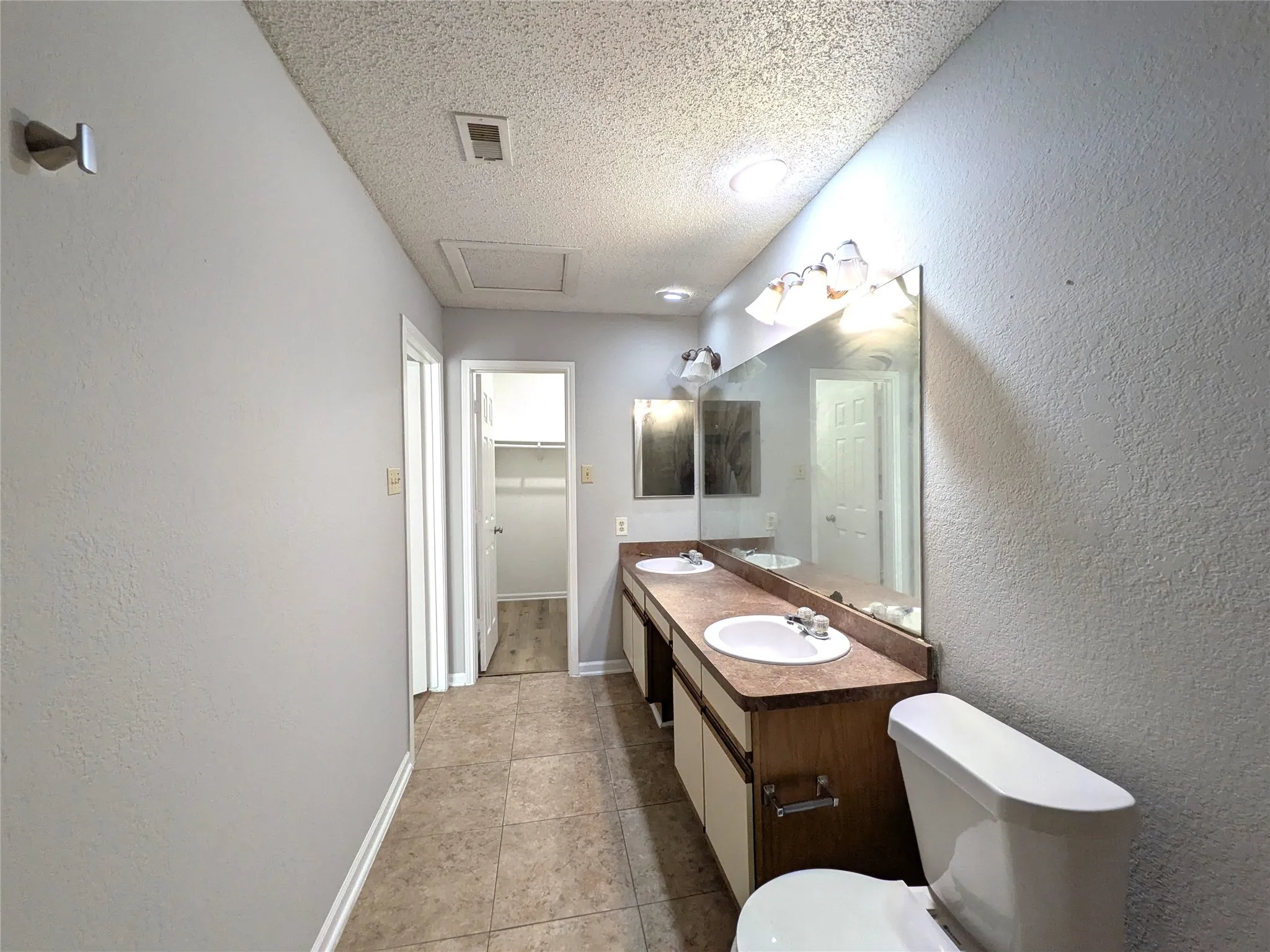 Dual vanity with integrated sinks and individual mirrors, overhead lighting, and tile flooring