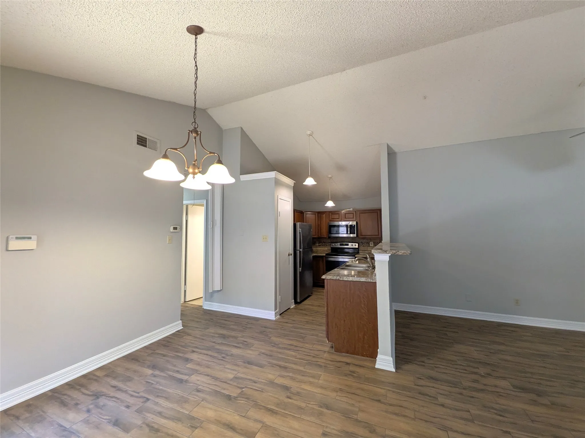 Vaulted ceiling, wood-finish flooring, kitchen with granite-style countertops, stainless steel appliances, and wood cabinetry
