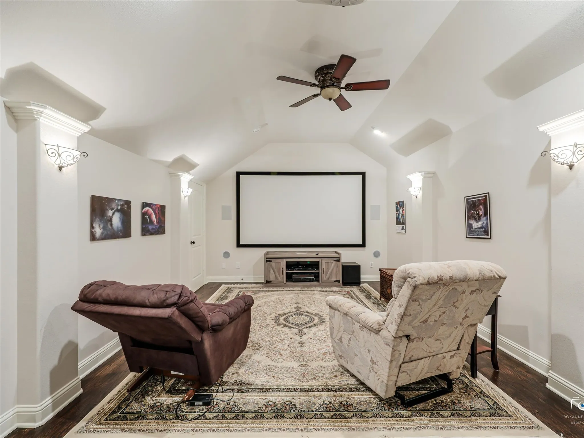 Media room featuring a projection screen, built-in speakers, decorative sconces, and a ceiling fan