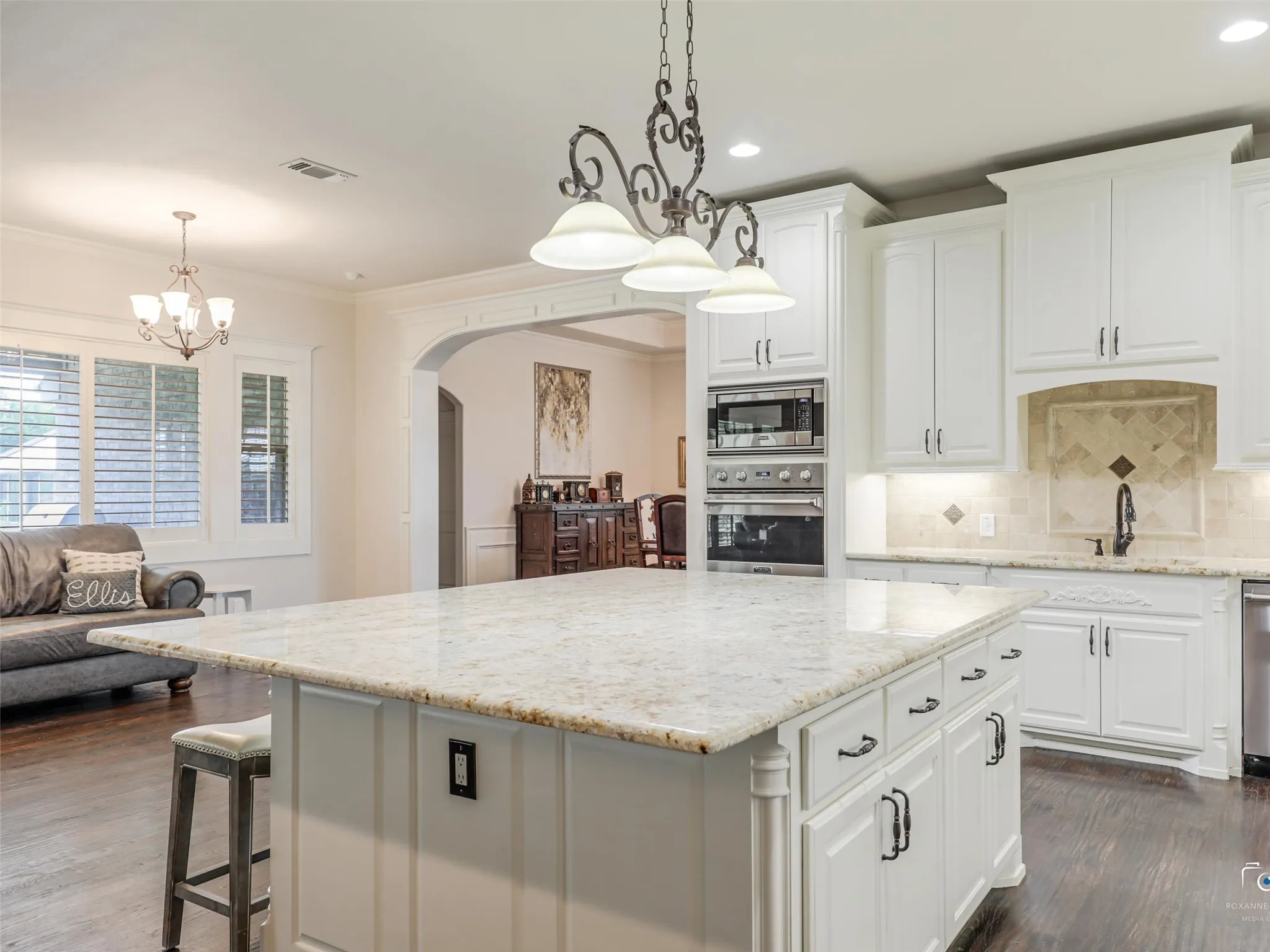 Gourmet kitchen featuring a large island with a light-toned countertop, white cabinetry with dark hardware, built-in stainless steel appliances, and a tiled backsplash