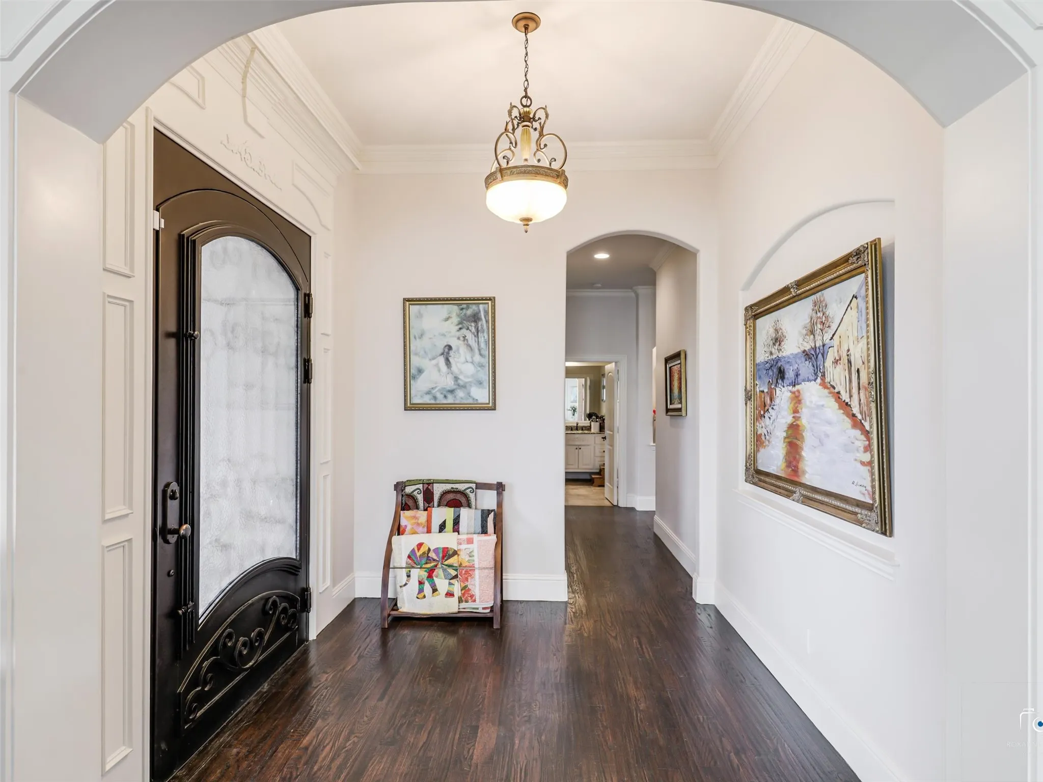 Arched entryways, dark wood-finish flooring, and crown molding
