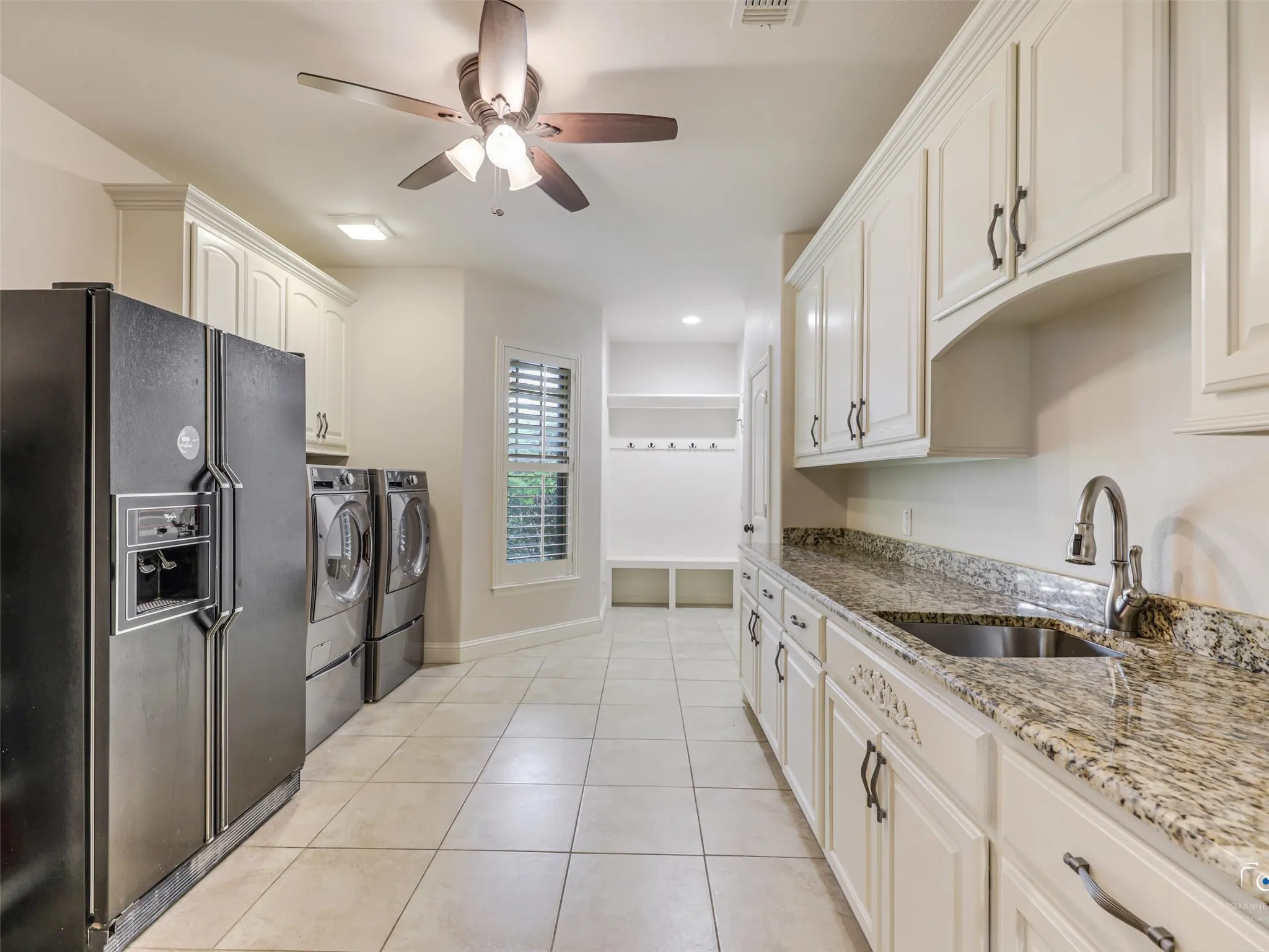 Spacious utility area featuring extensive cabinetry, stone countertops, a stainless steel sink, tiled flooring, and a ceiling fan