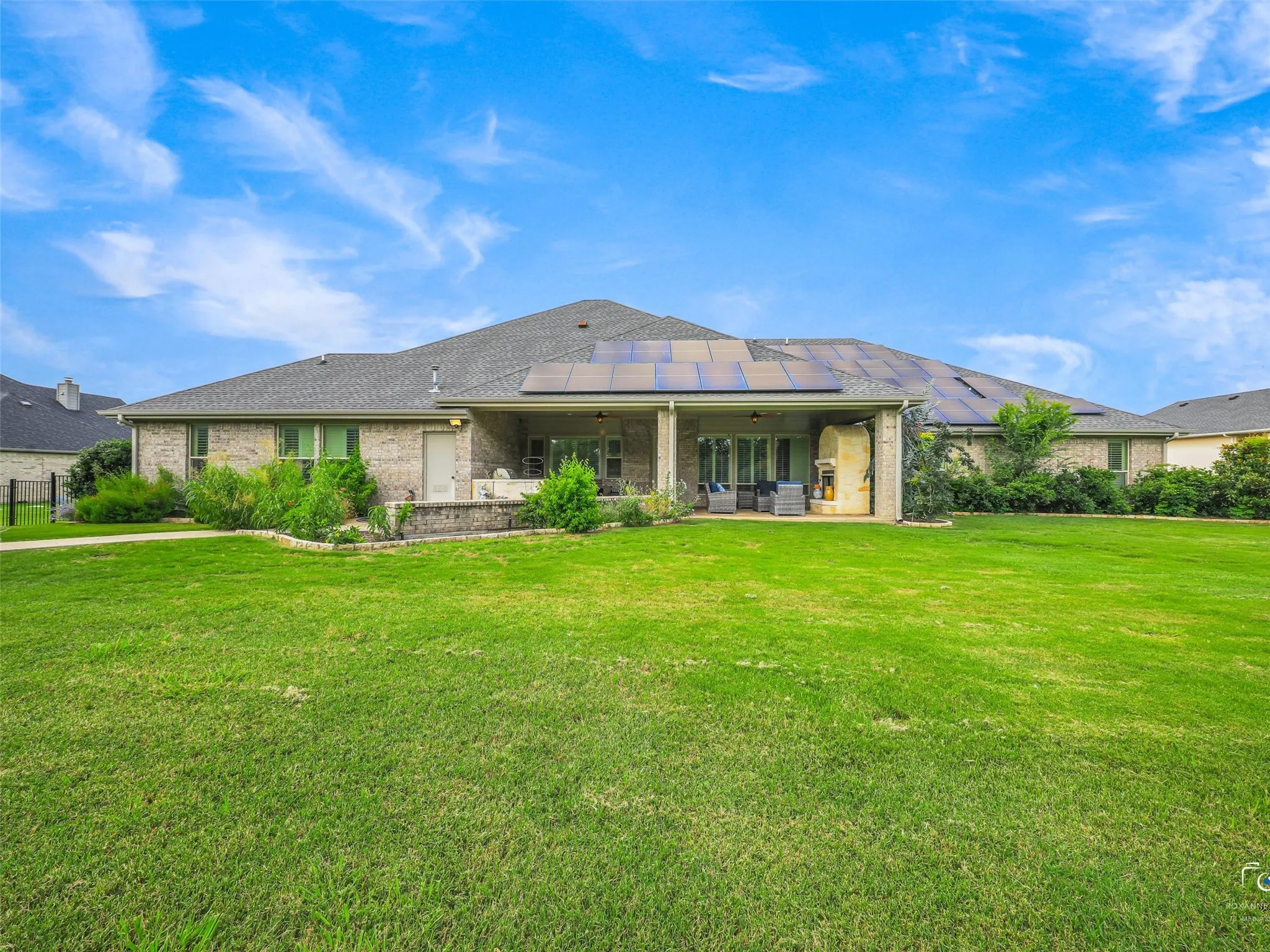 Expansive green lawn with a brick exterior, covered patio, and roof-mounted solar panels