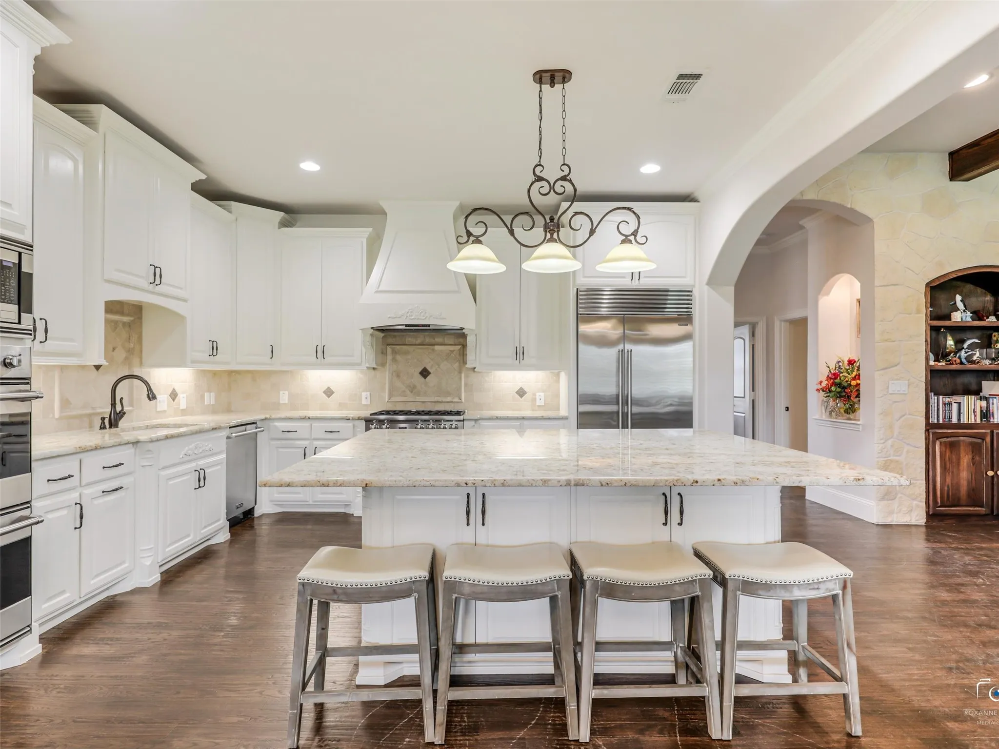 Gourmet kitchen featuring white cabinetry, stainless steel appliances, a large center island with stone countertops, dark wood-finish flooring, and arched architectural details