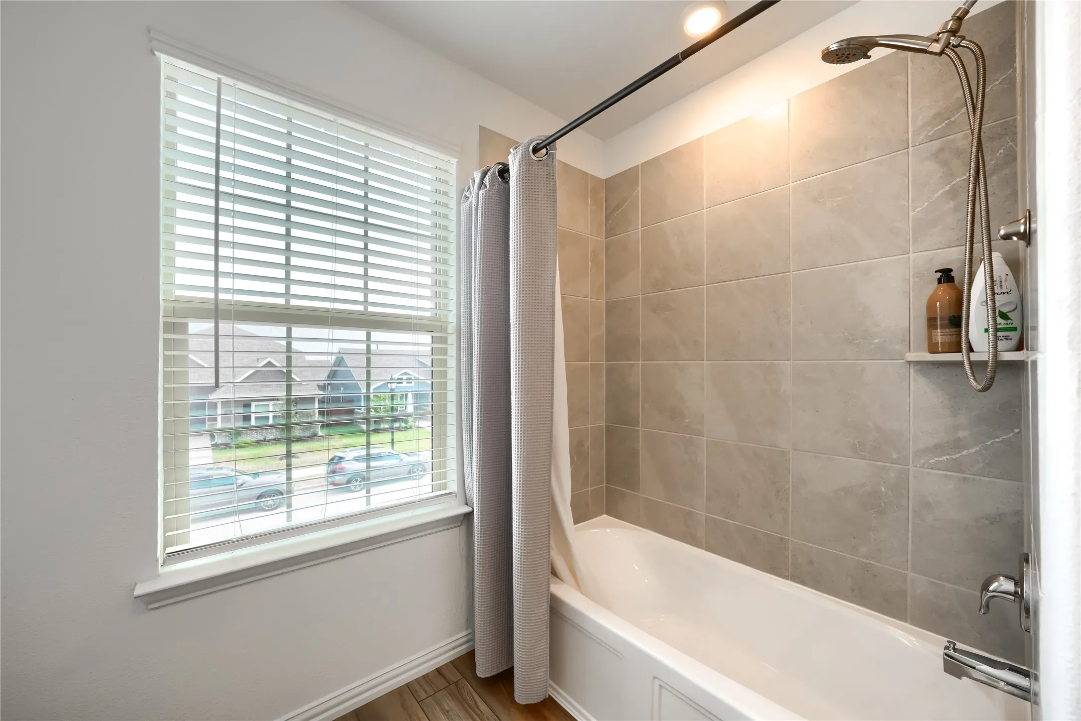 Bathtub with a tiled surround, integrated shower niche, and a showerhead with a handheld sprayer