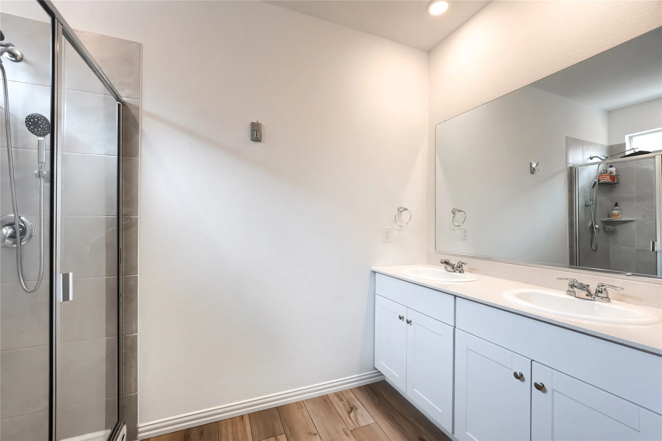 Spacious bathroom with wood-finish flooring, a dual-sink vanity, and a glass-enclosed shower with tiled walls
