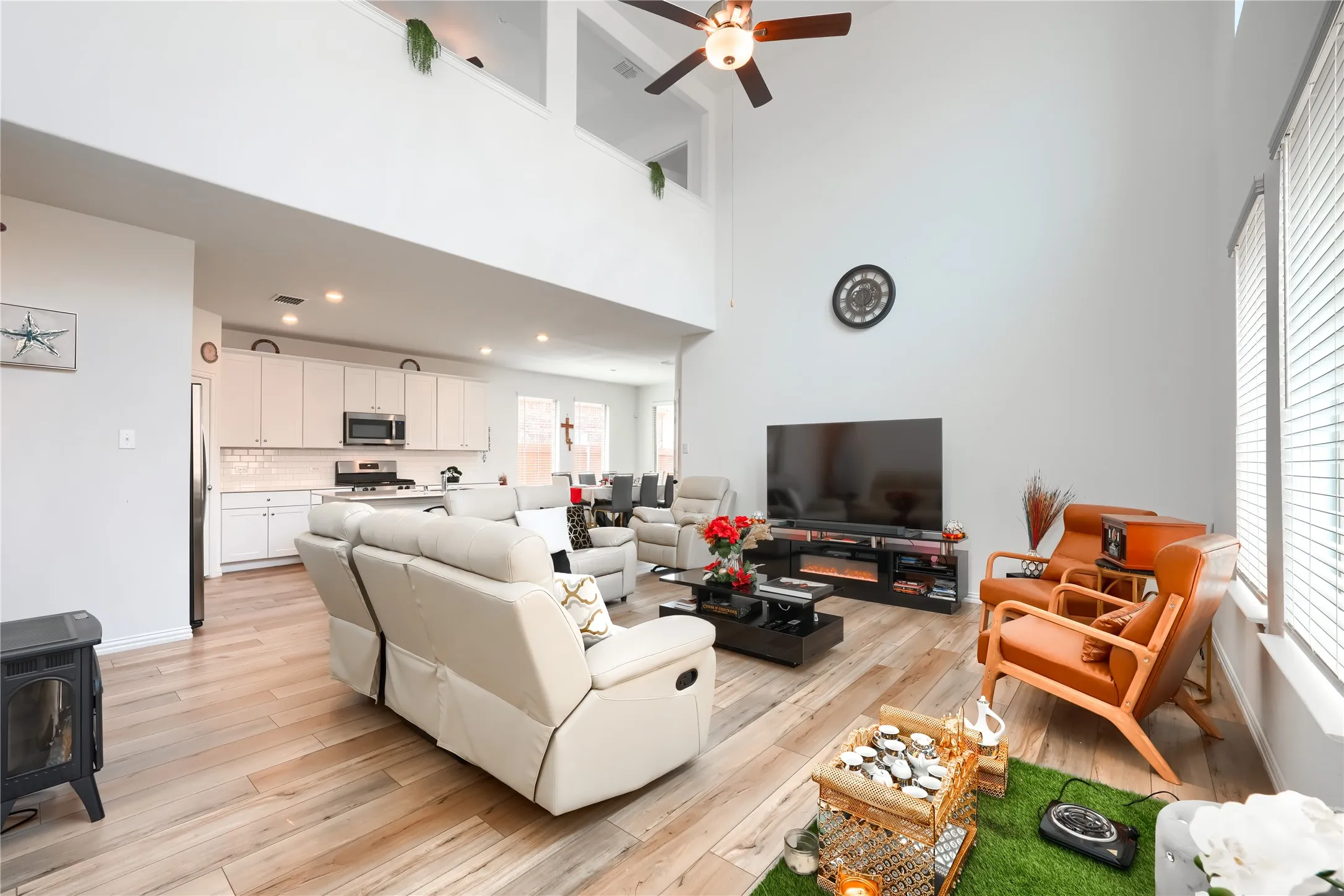 Open-concept living area featuring soaring vaulted ceilings with ceiling fan, wood-finish flooring throughout, and abundant natural light from large windows