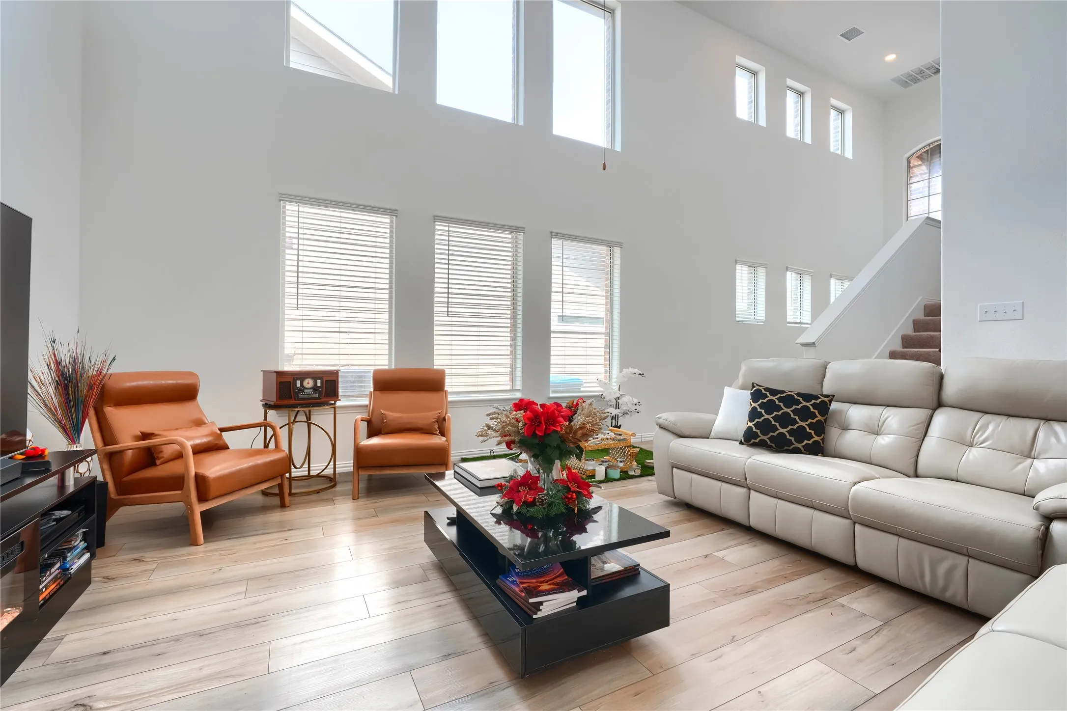 Two-story living area with high ceilings, multiple windows, and wood-finish flooring