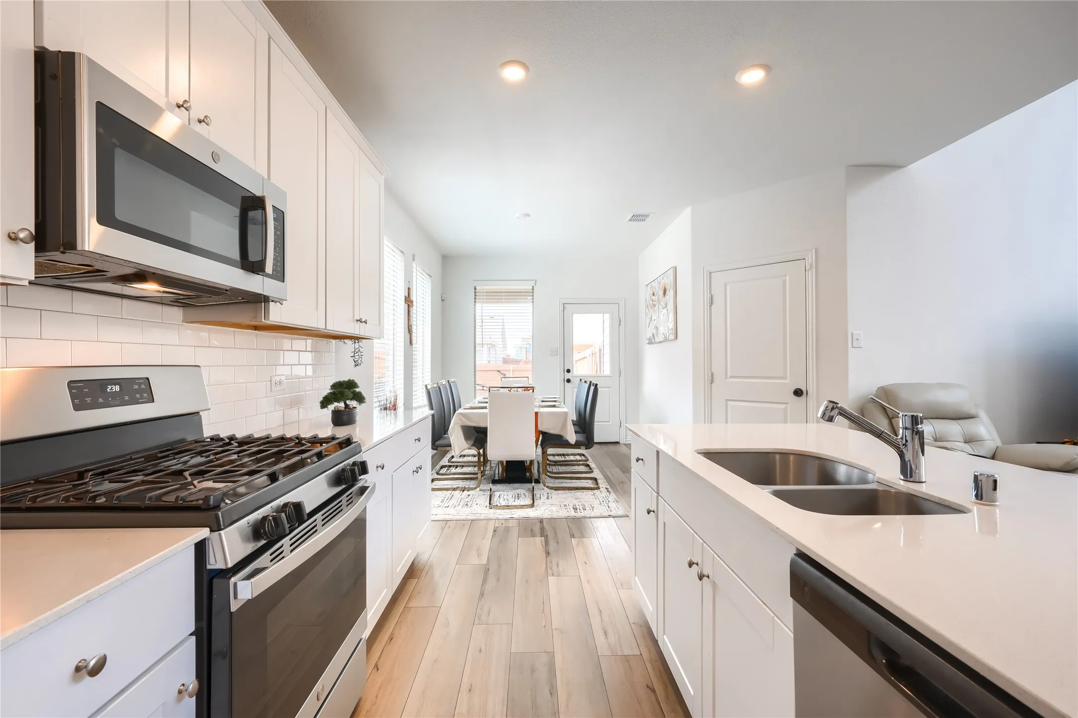 Contemporary kitchen featuring stainless steel appliances, white cabinetry, a dual basin sink, light wood-finish flooring, and recessed lighting
