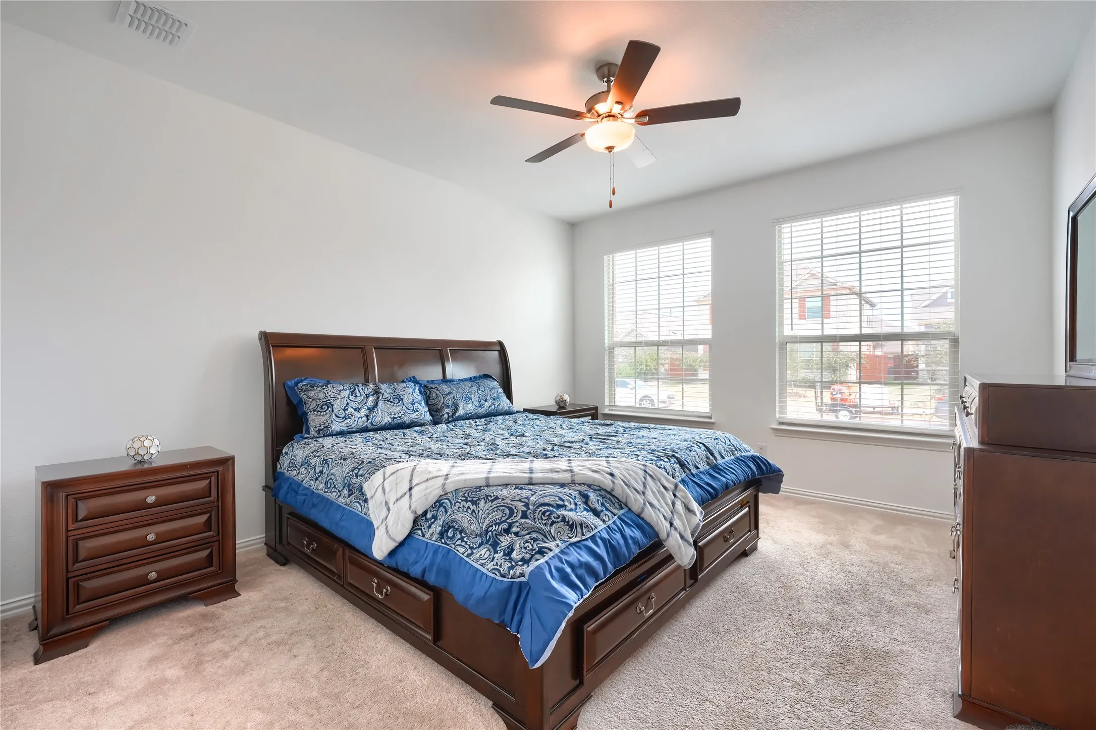 Plush carpeting, two large windows, and a ceiling fan with integrated lighting
