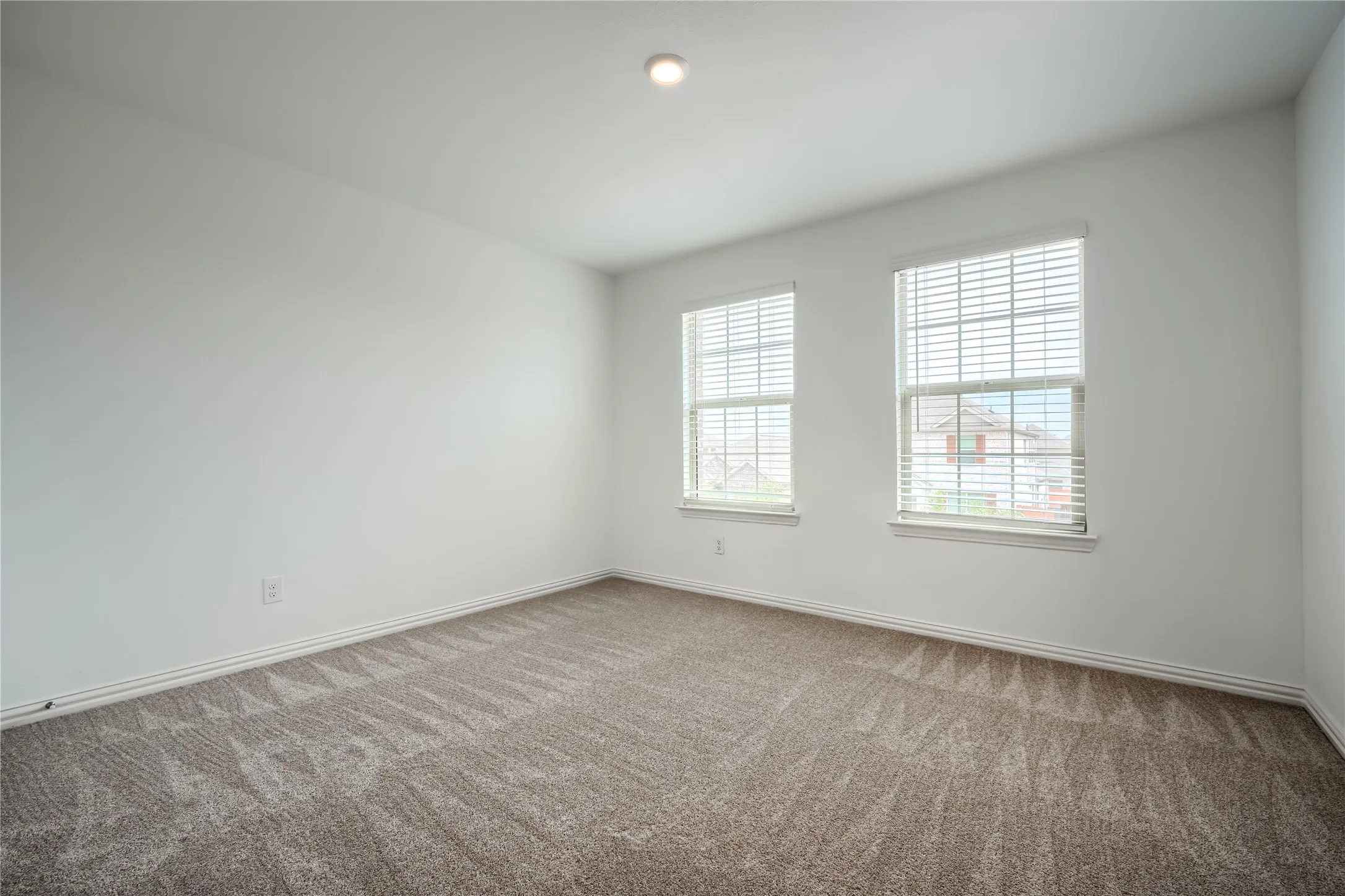 Neutral wall paint, two windows with blinds, recessed ceiling lighting, and textured carpeting