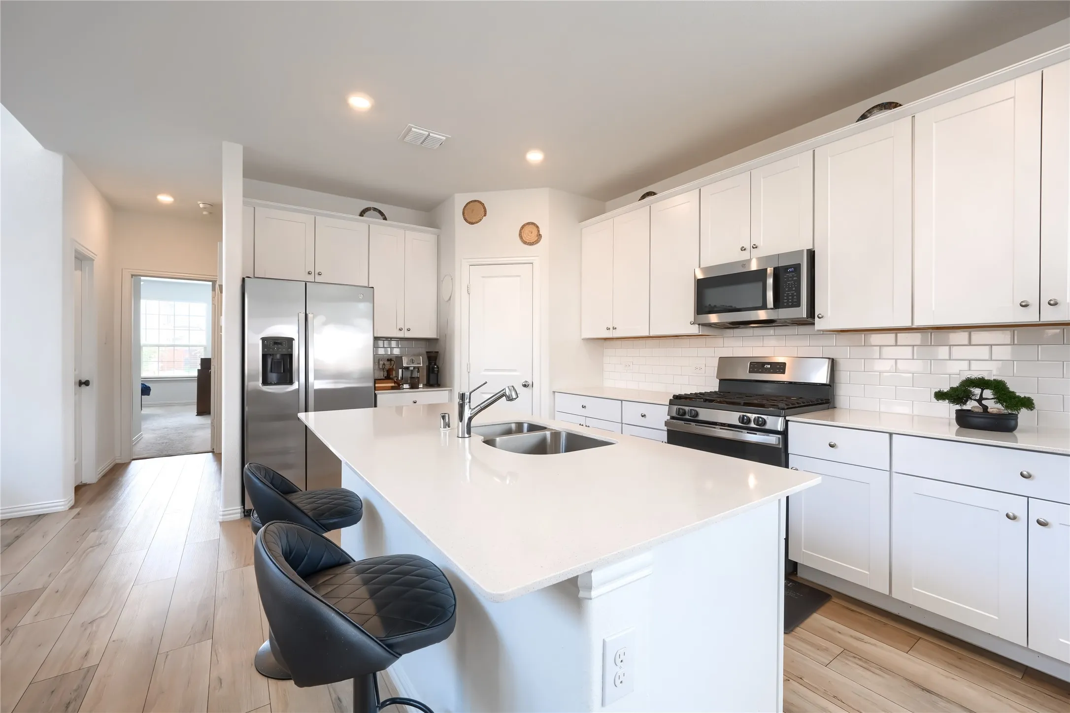 Kitchen featuring an expansive center island with an undermount double sink, white shaker-style cabinetry, stainless steel appliances, and wood-finish flooring