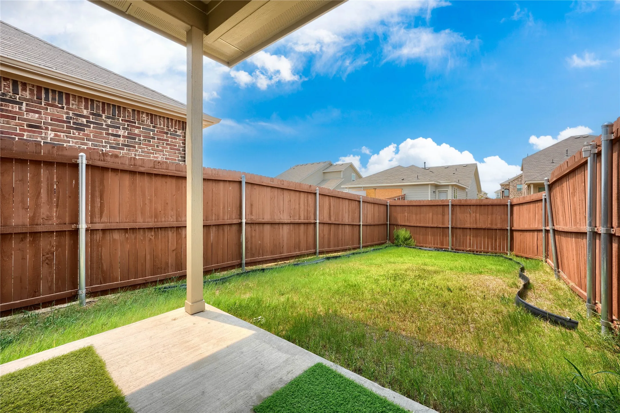 Covered patio with concrete flooring, private wood fencing, and a grass lawn