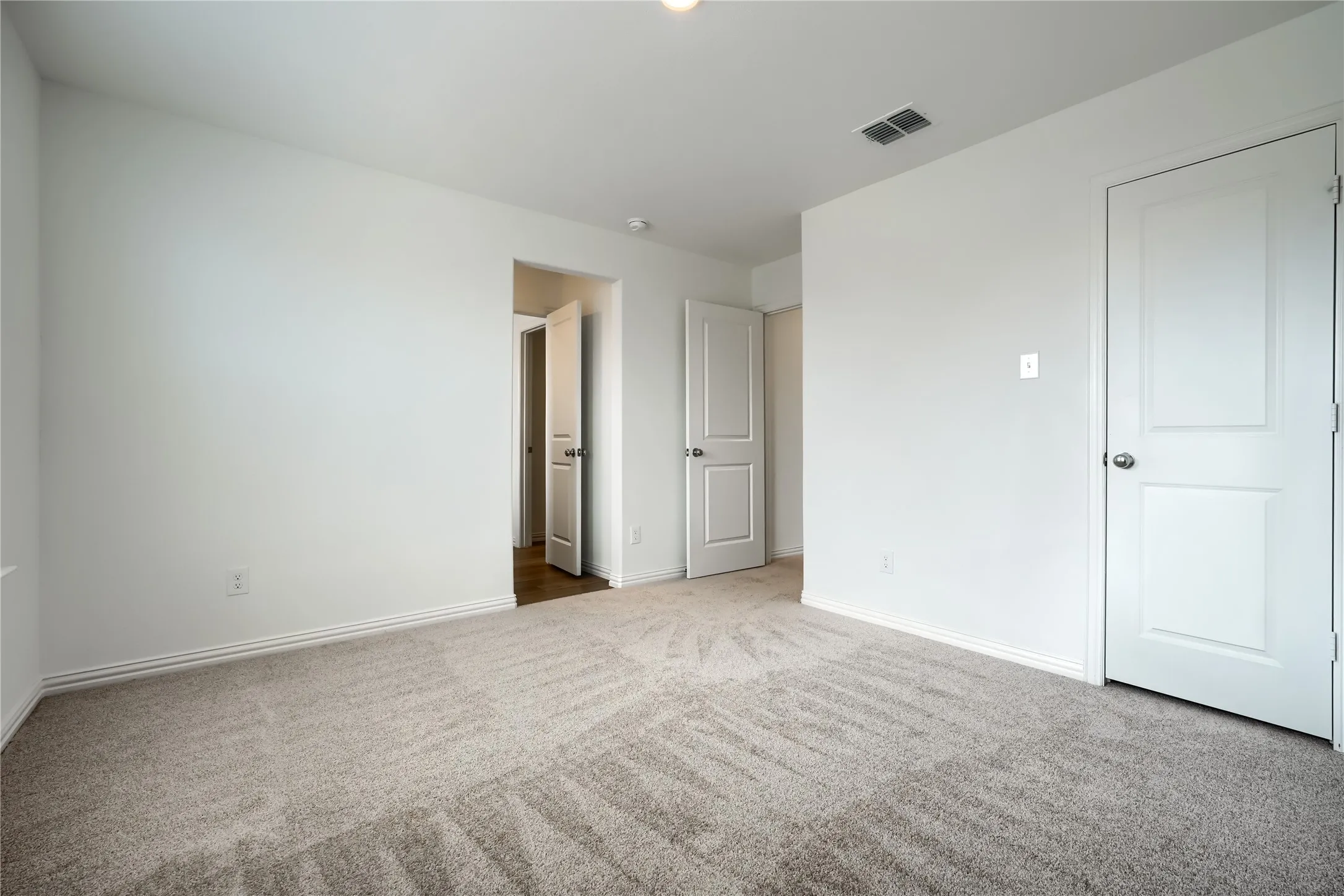 Spacious bedroom with neutral wall finishes, carpet flooring in a linear pattern, and multiple white six-panel doors providing access to closet and hallway spaces