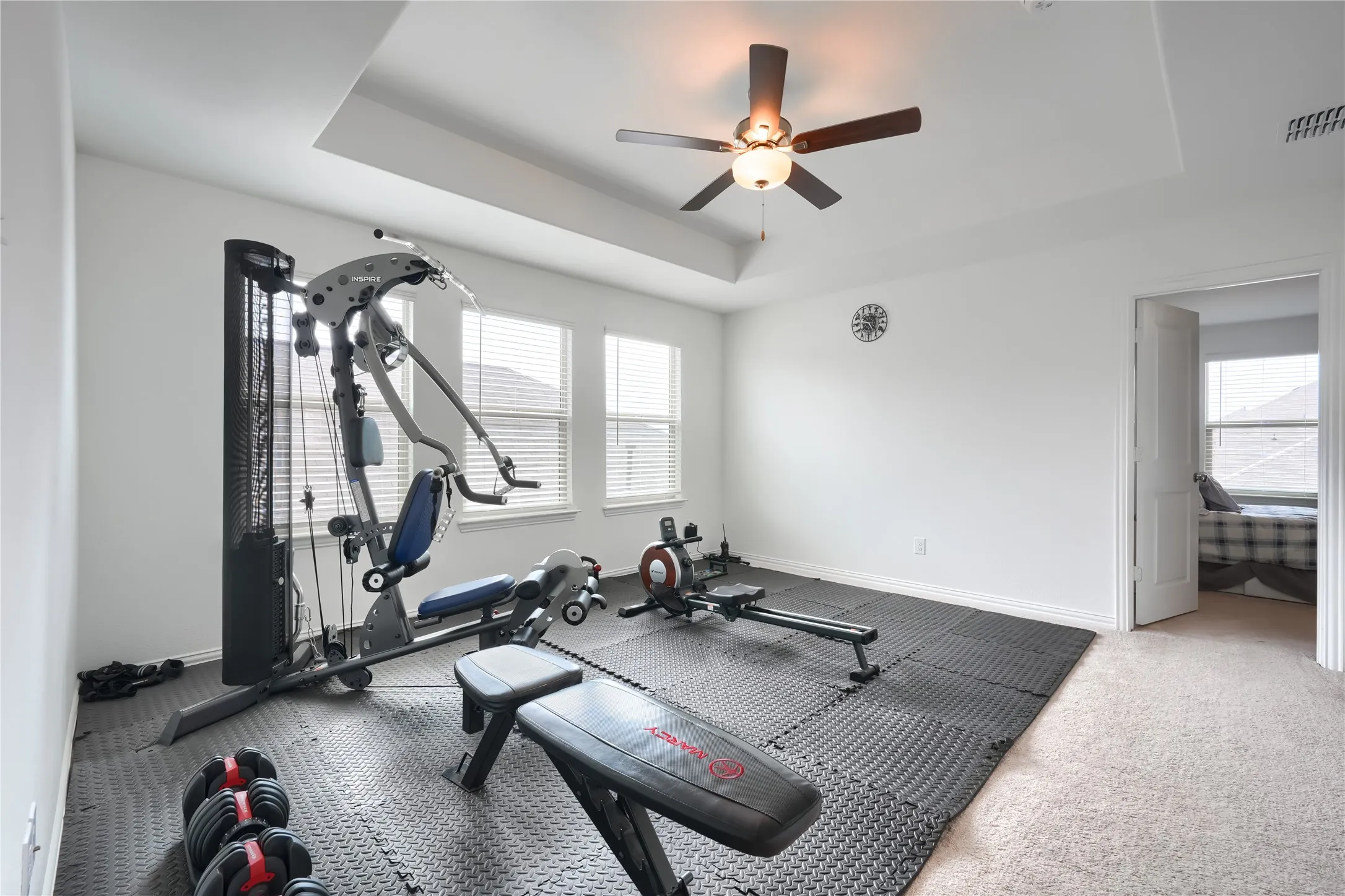 Tray ceiling with a ceiling fan, multiple windows with blinds, and light-colored carpet flooring