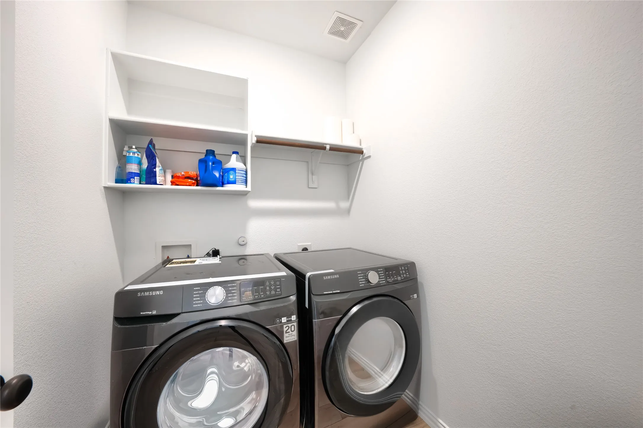 White laundry room with wall-mounted shelving, overhead ventilation, and a wood-finish rod