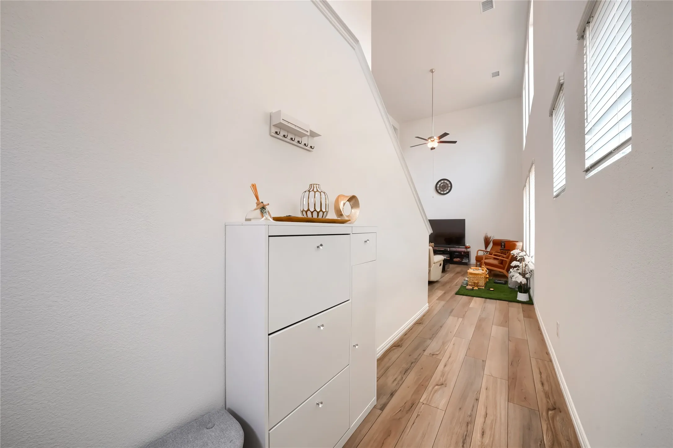 Vaulted ceiling with a ceiling fan, multiple windows with blinds, and wood-finish flooring