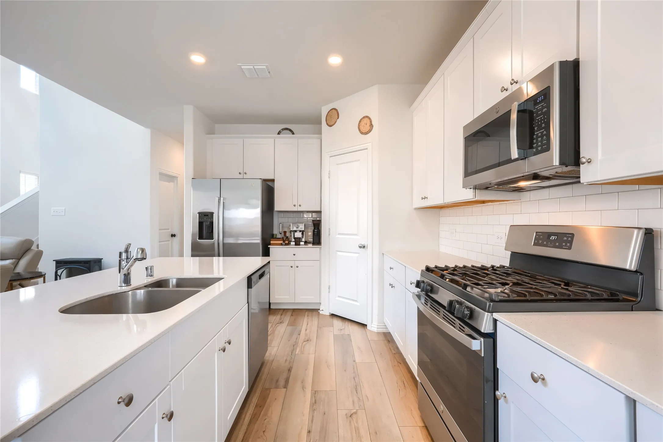 Kitchen featuring white cabinetry, stainless steel appliances, light-toned wood-finish flooring, white countertops, and a subway tile backsplash