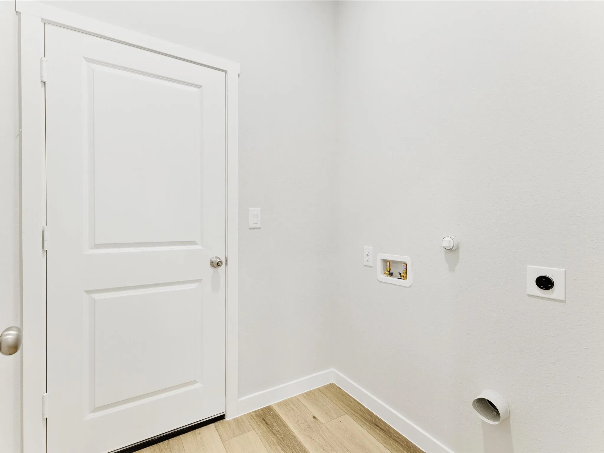 Laundry area with wood-finish flooring, white paneled door, and utility hookups