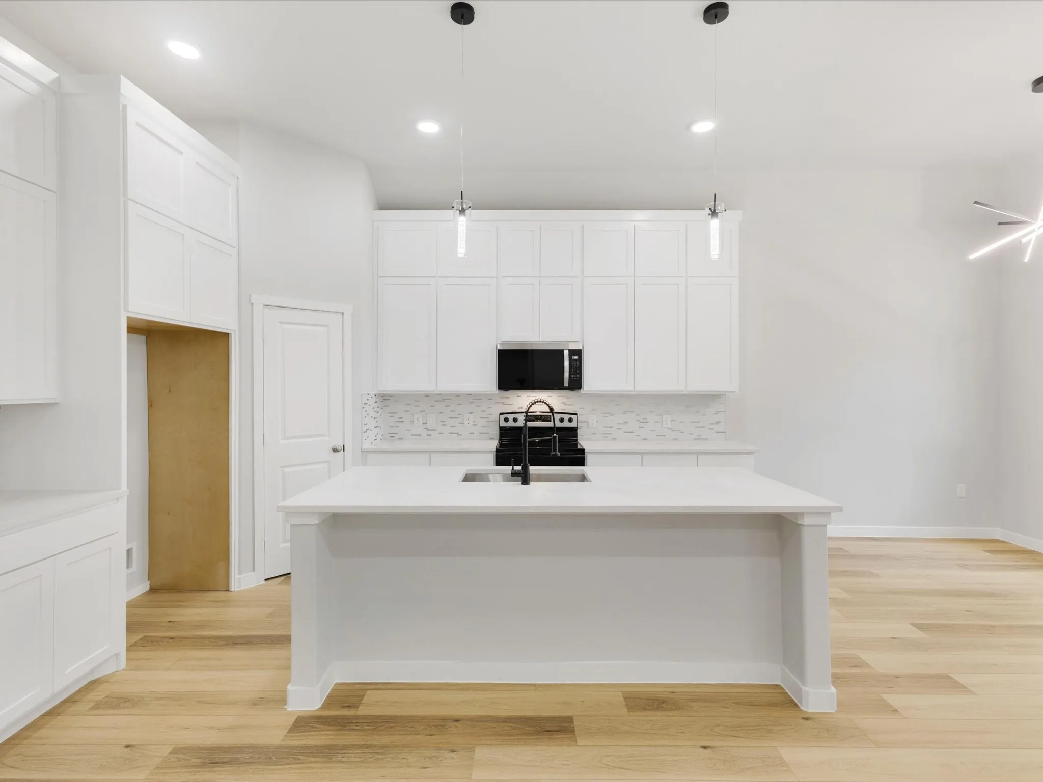 Modern kitchen featuring white cabinetry, light wood-finish flooring, a kitchen island with a built-in sink, and a tile backsplash