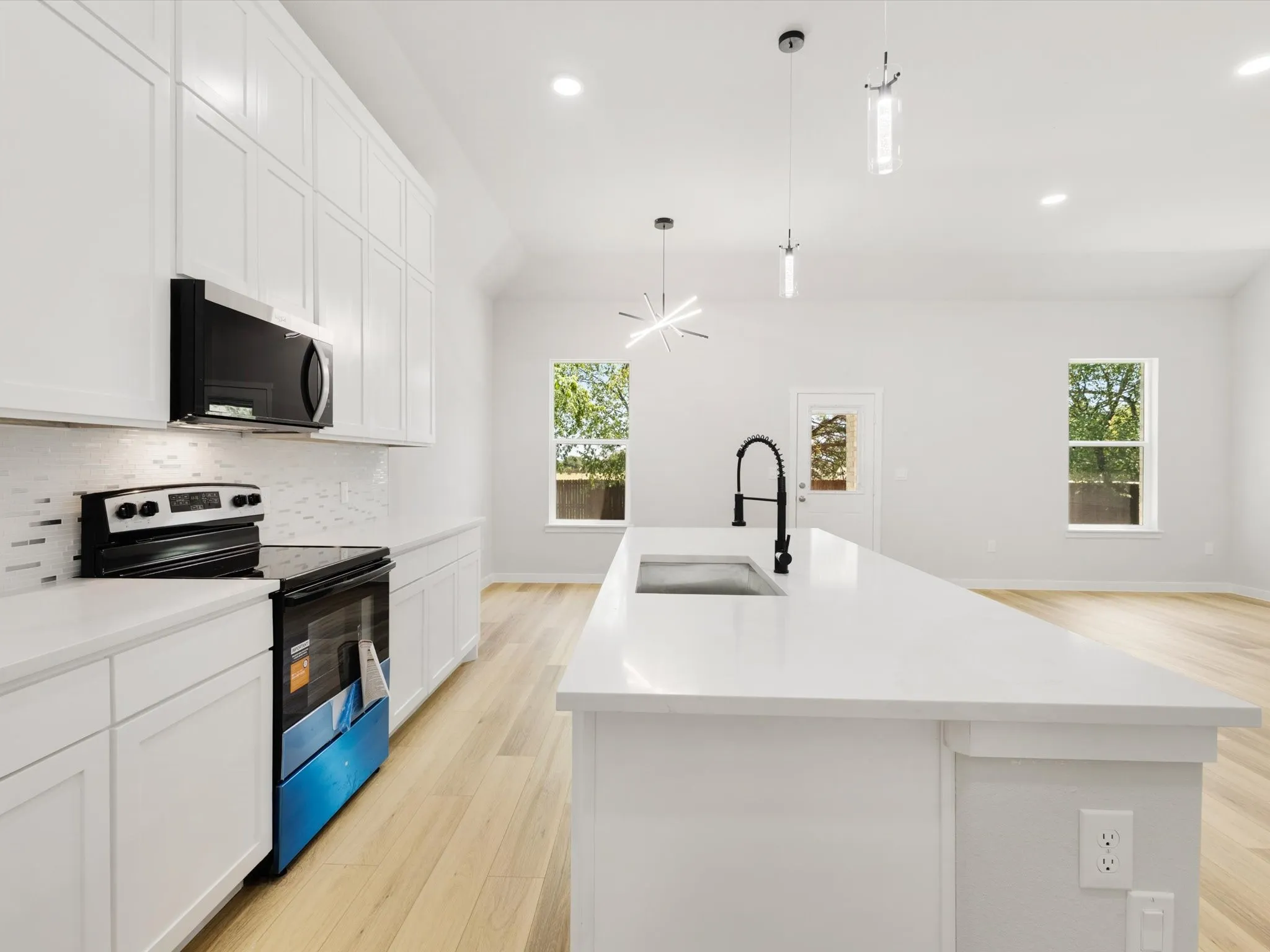 White shaker cabinetry, quartz countertops, wood-finish flooring, recessed lighting, and a kitchen island with sink and modern pendant lighting