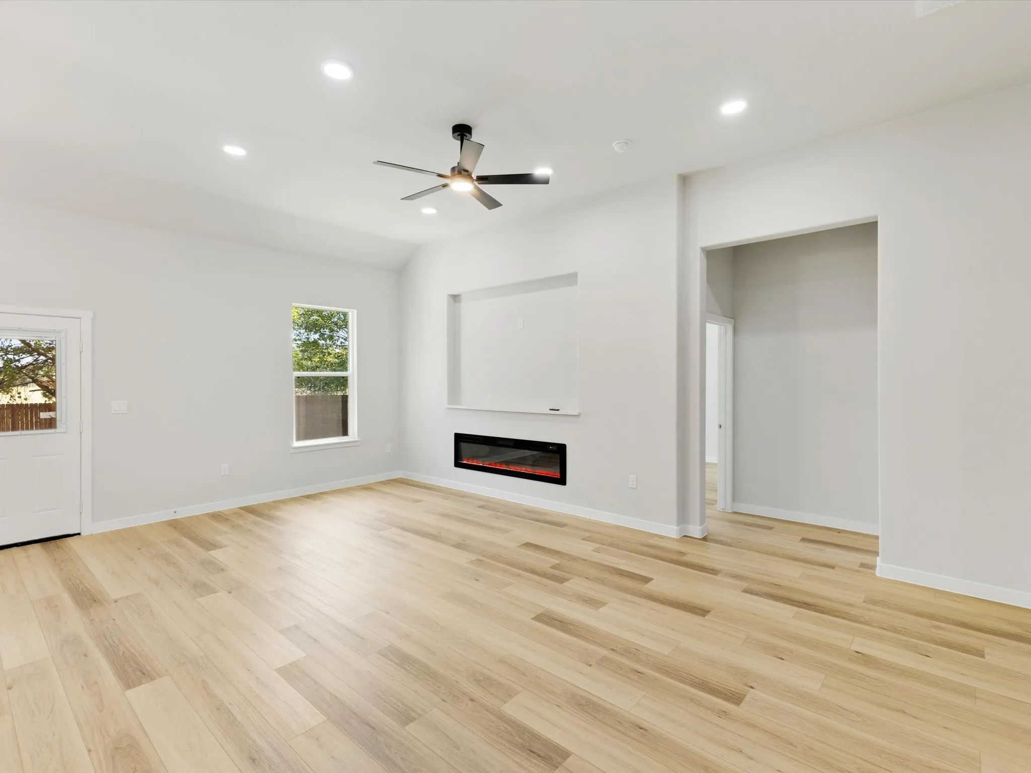 Vaulted ceiling with recessed lighting, wood-finish flooring, and an electric fireplace with built-in shelving