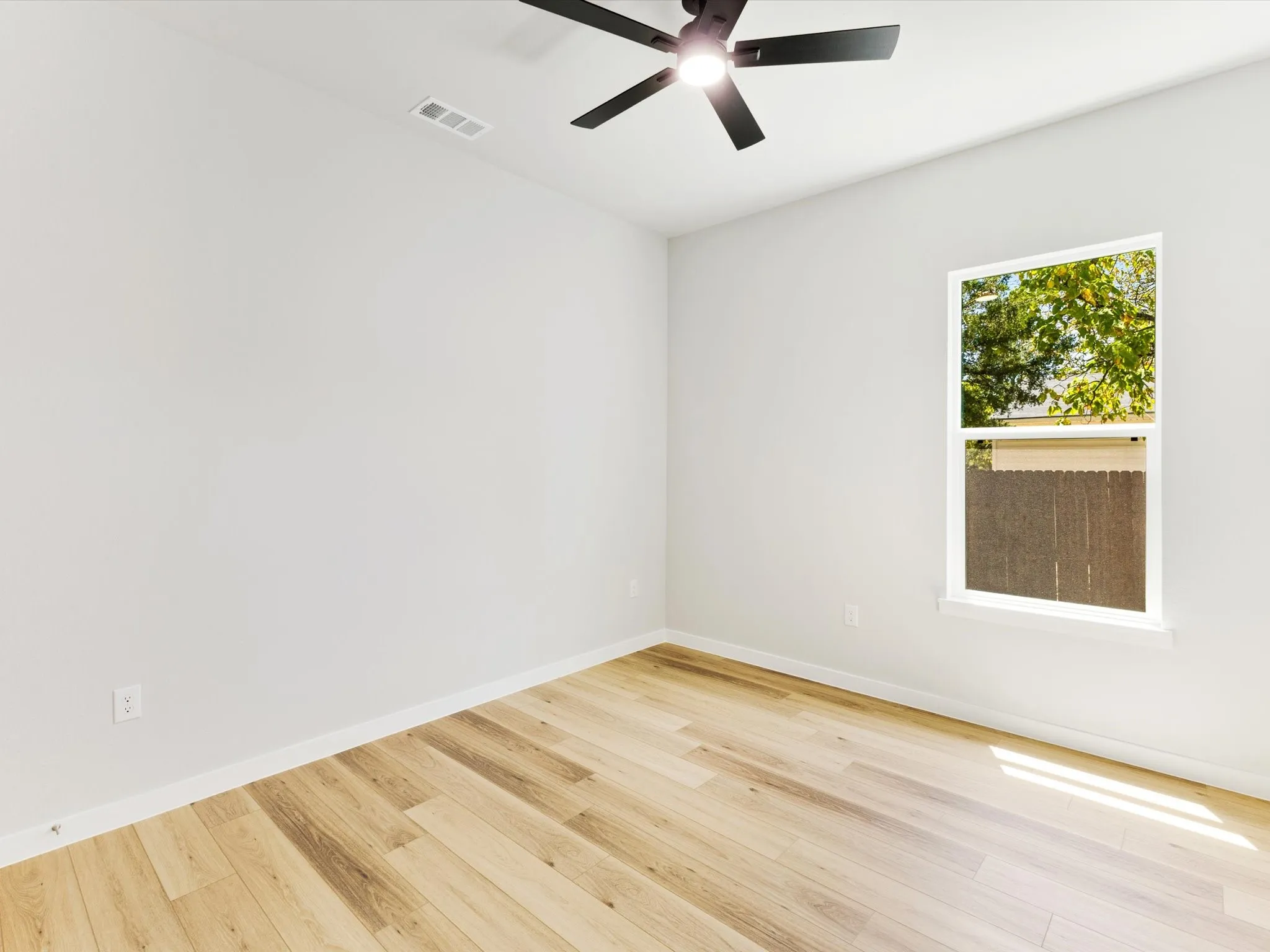 Wood-finish flooring, single window, white walls, and a ceiling fan with integrated lighting