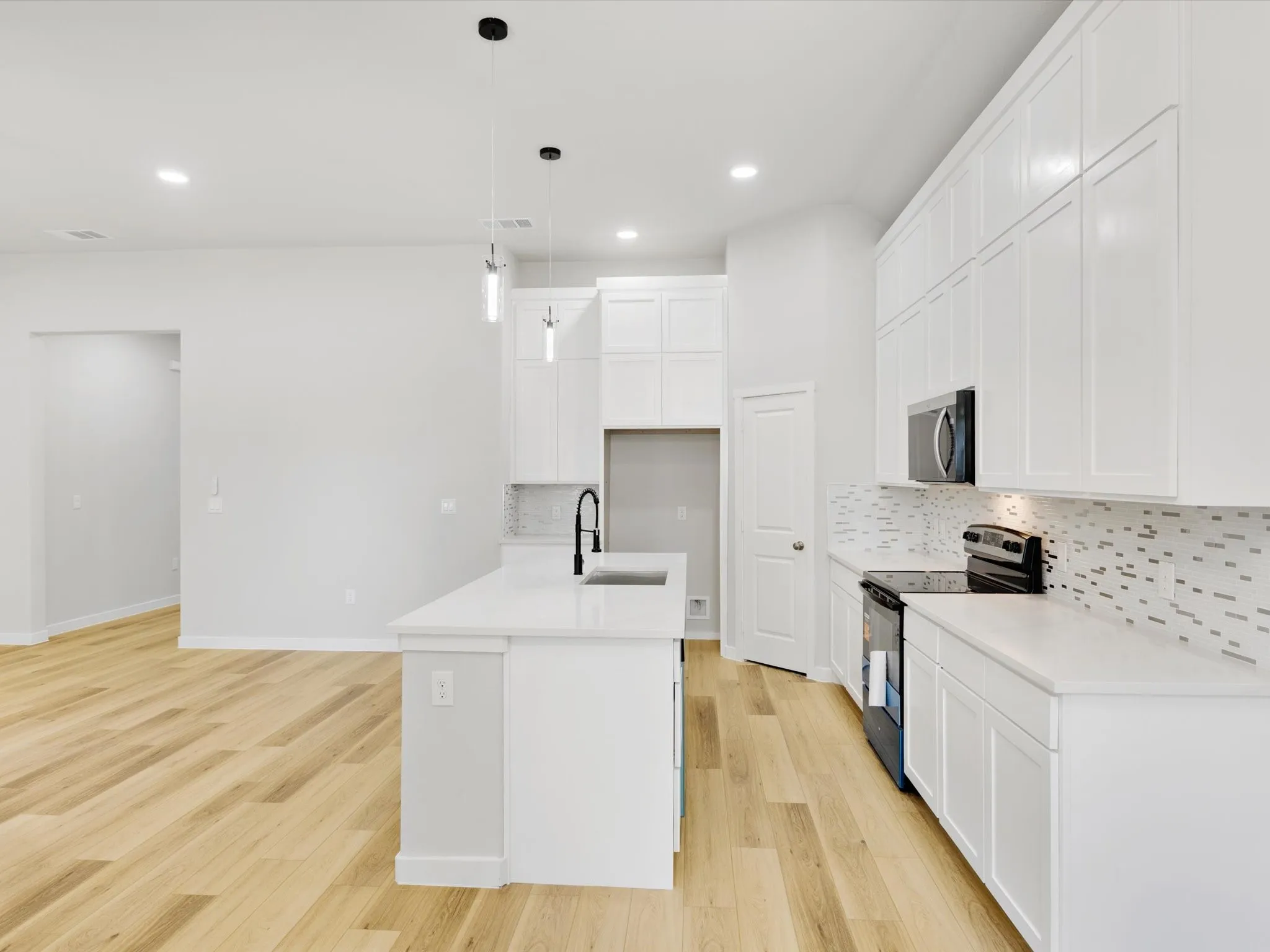 Kitchen featuring a central island, white cabinetry, integrated microwave, contemporary pendant lighting, and wood-finish flooring