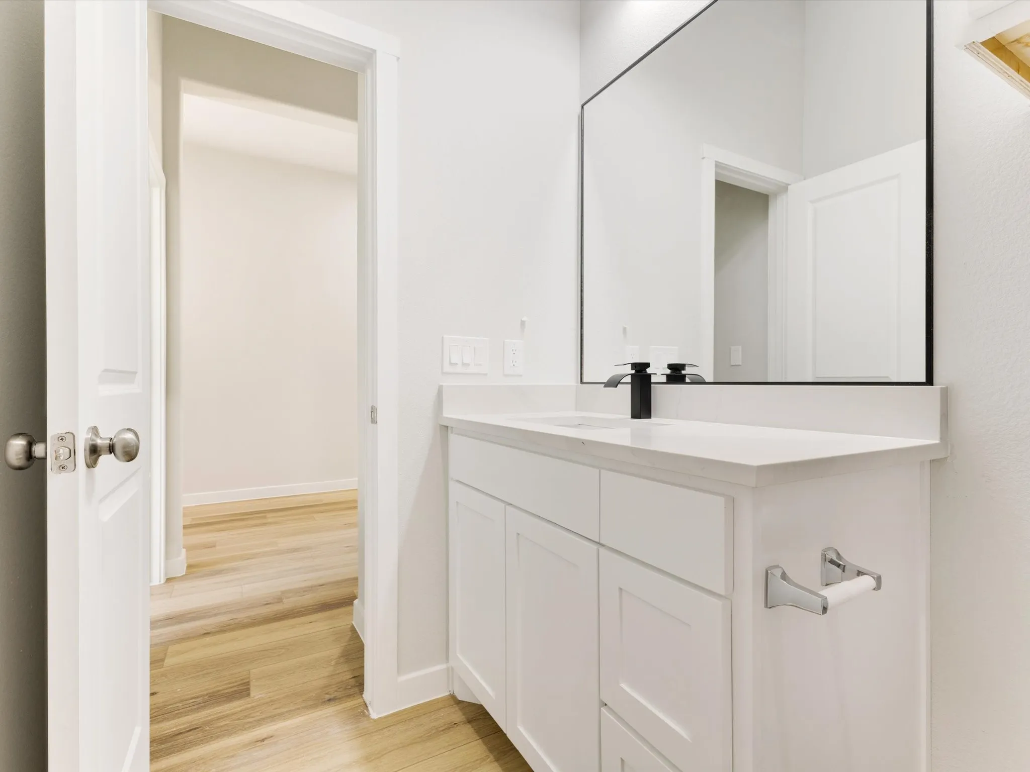 White vanity with integrated sink, black framed mirror, wood-finish flooring, and matte black faucet