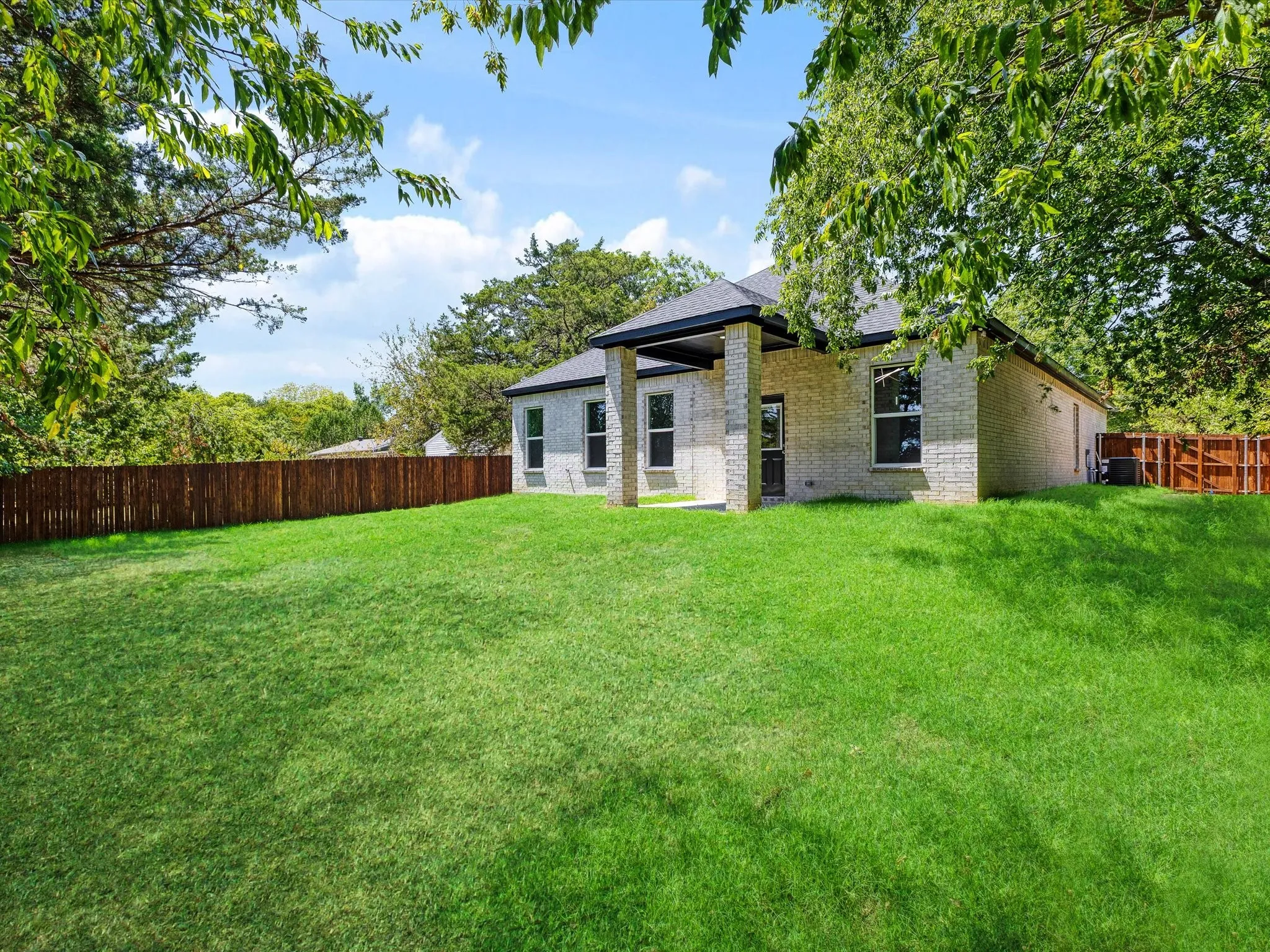 Spacious lawn area with a wood privacy fence, featuring a light-colored brick exterior and a covered patio with columns