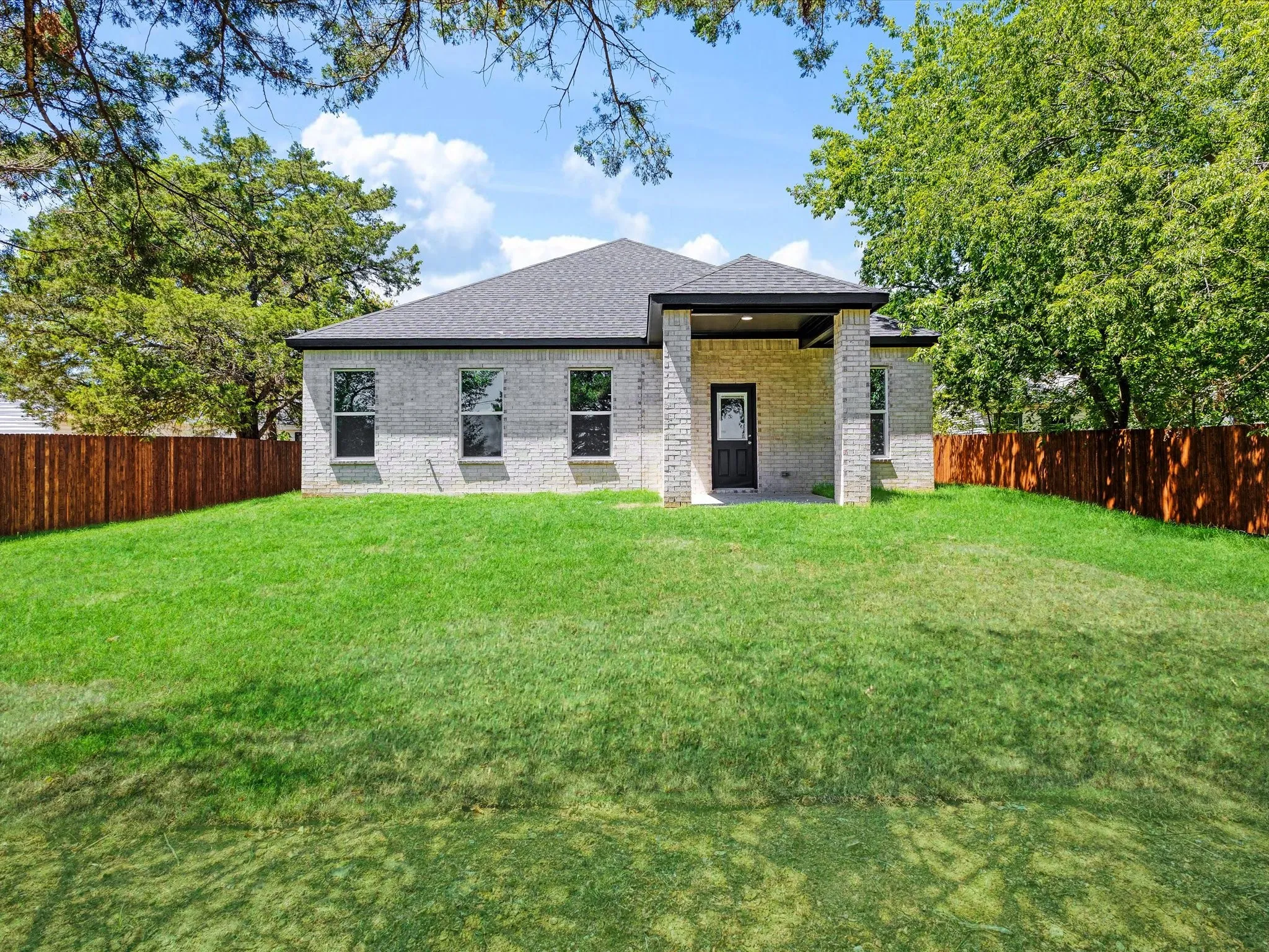 Brick exterior with a covered patio, dark roof shingles, and a privacy fence