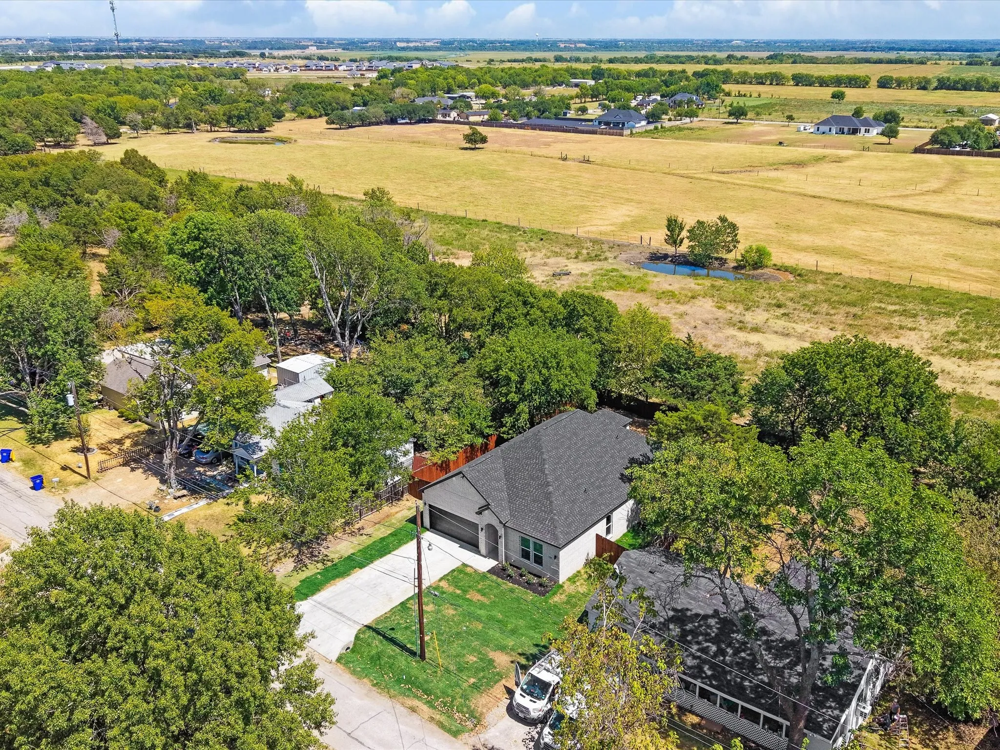 Expansive lot featuring mature trees, a long driveway, a private backyard with a wood fence, and a distant pond