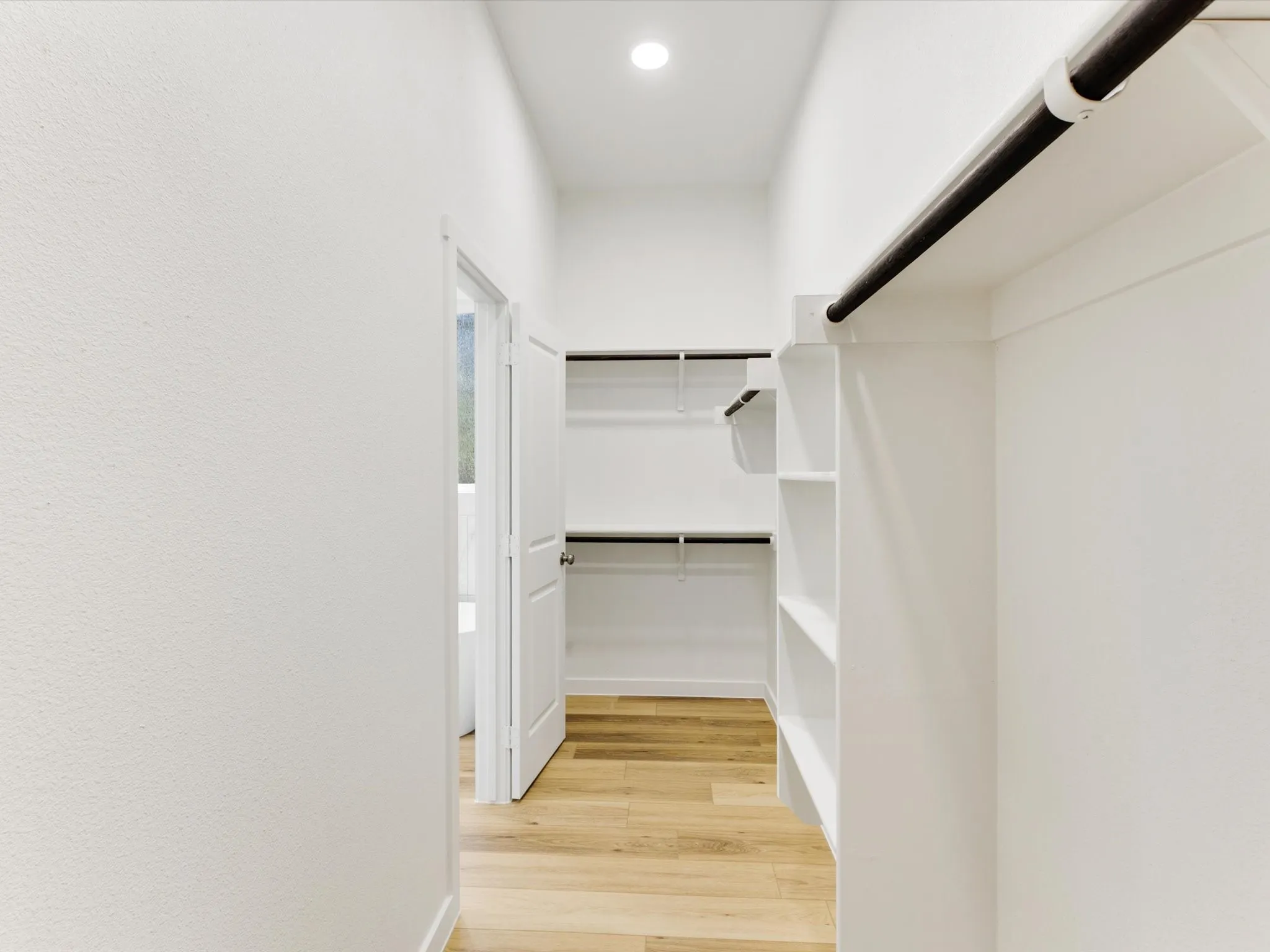 Walk-in closet featuring wood-finish flooring, recessed lighting, white built-in shelving, and hanging rods