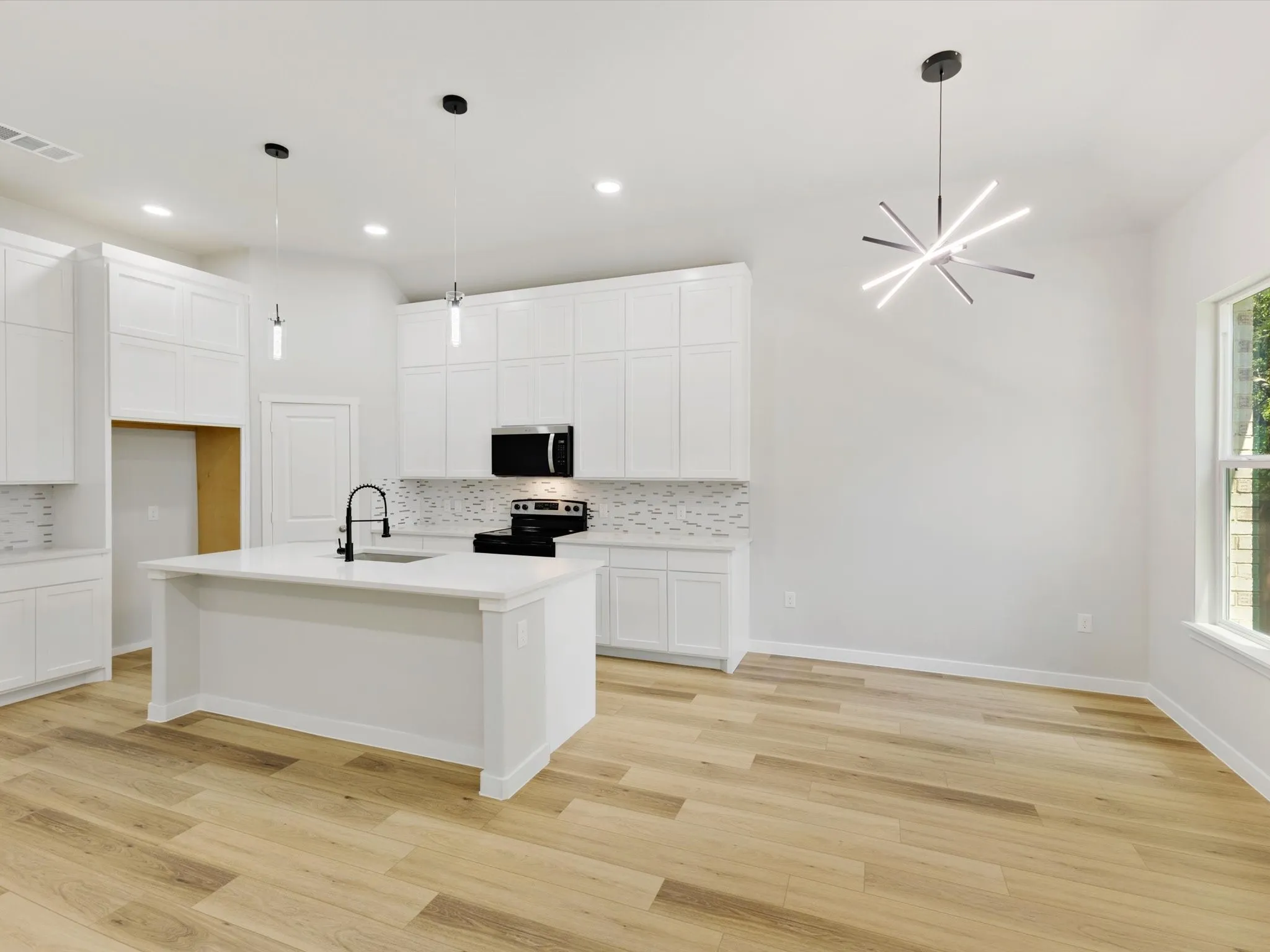 White shaker cabinetry, wood-finish flooring, island with integrated sink, contemporary pendant lighting, and stainless steel appliances