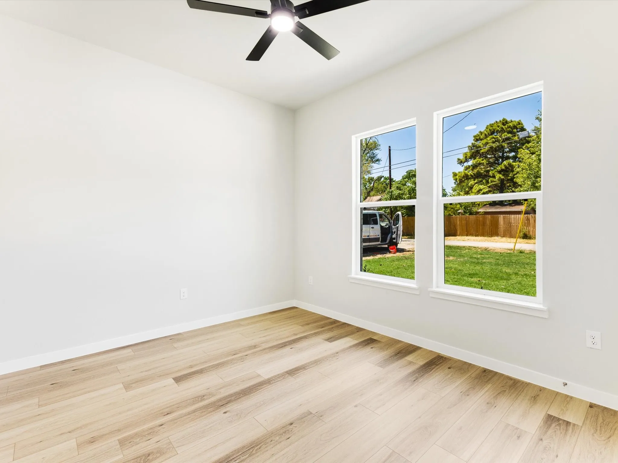 Light-toned wood-finish flooring, white walls, and a black ceiling fan with integrated lighting