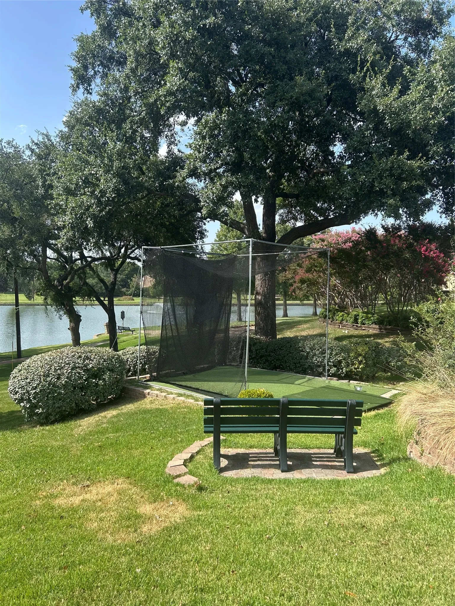 Lush green lawn with a golf net, artificial turf putting area, and a dark green slatted bench