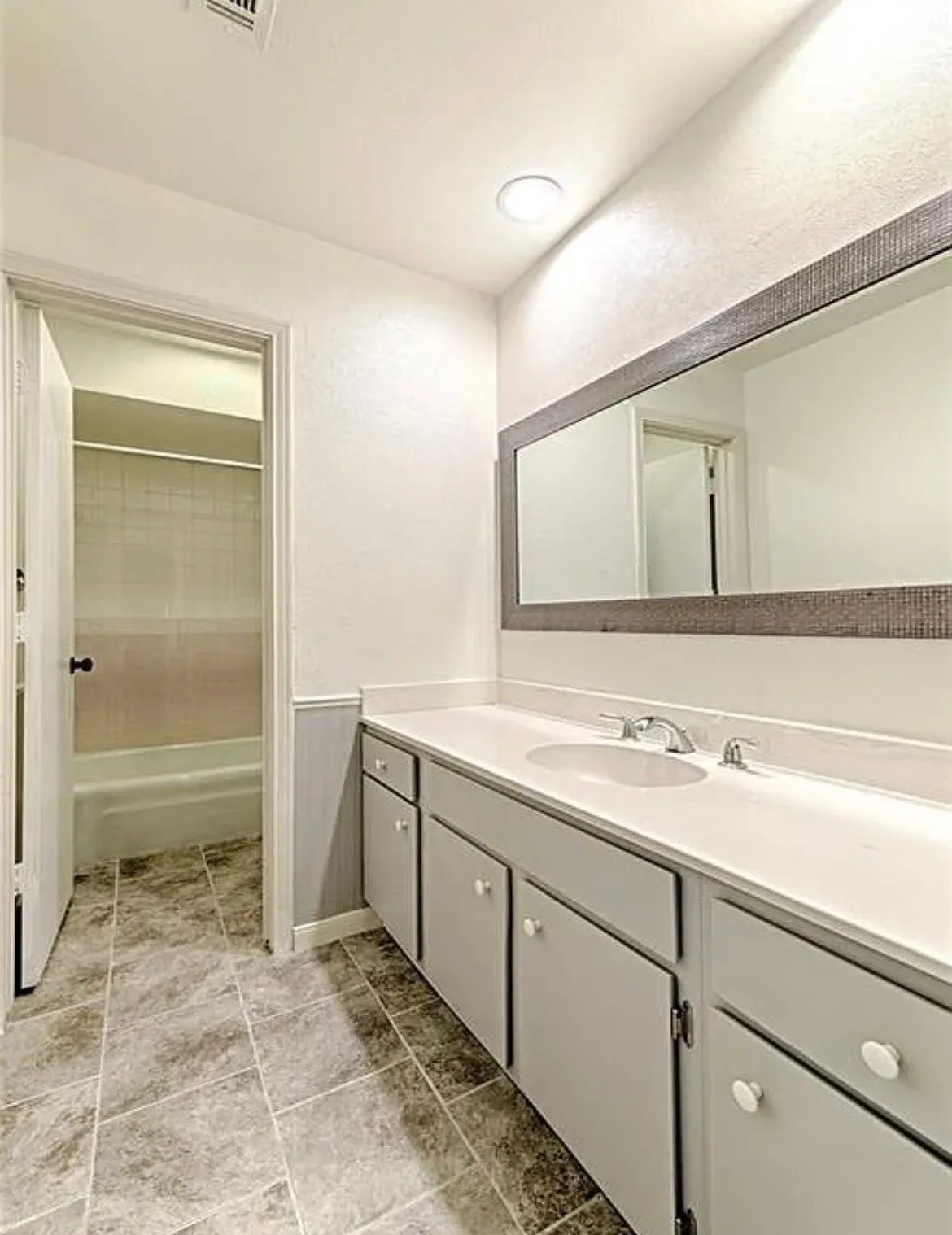 Dual basin vanity with white countertop and cabinetry, tile flooring, and a large mirror with a textured frame